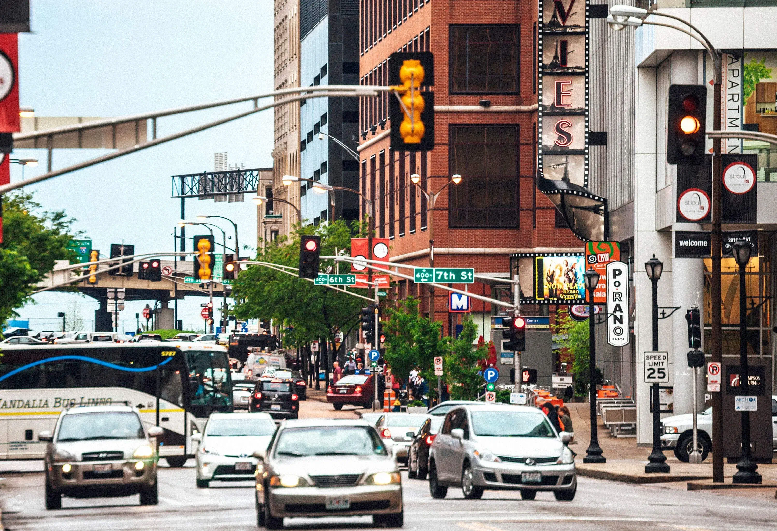 Cars moving through a busy street studded with directional signs, traffic lights, and huge buildings.