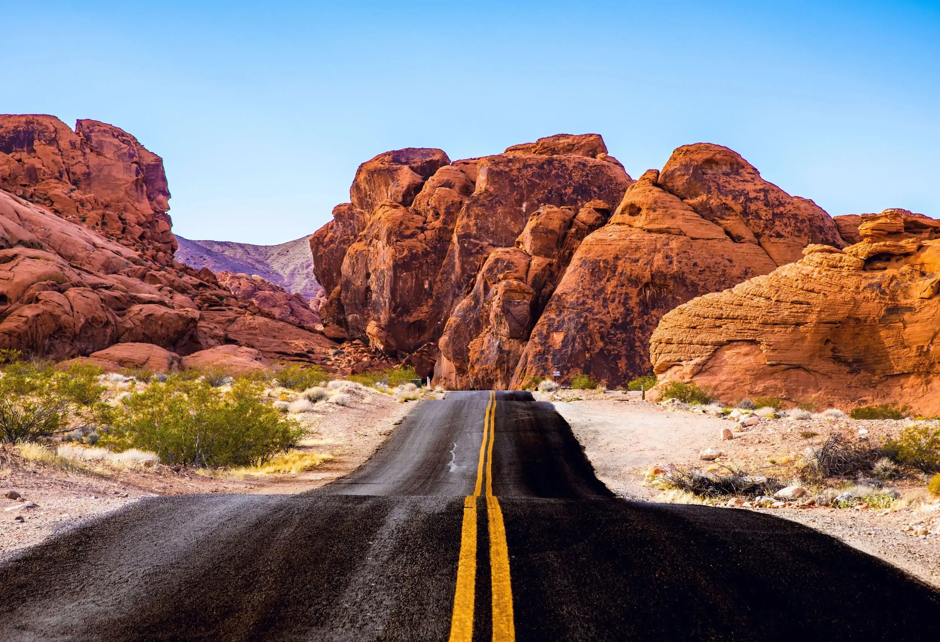 An undulating asphalt road that winds its way between red rock formations.