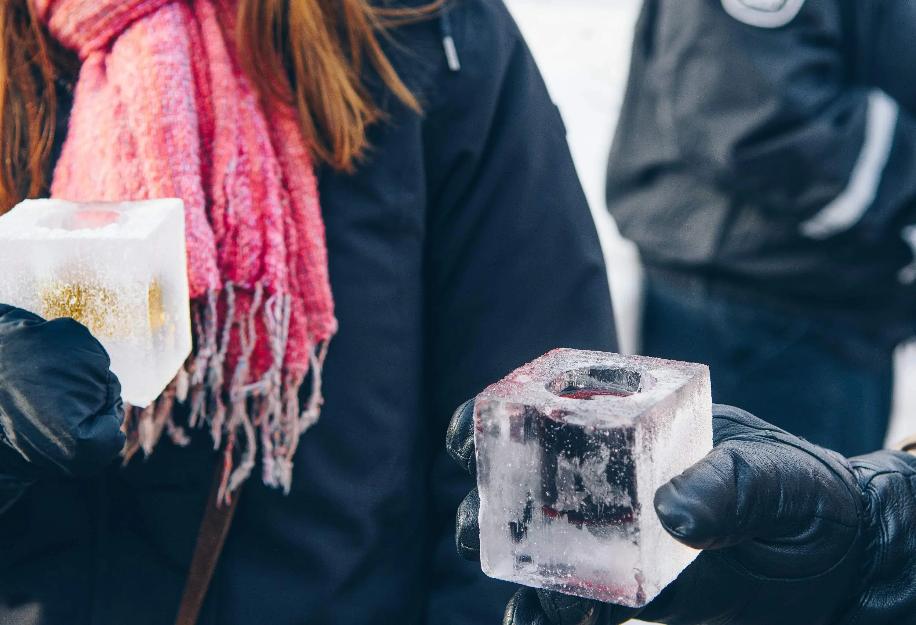 Two friends in winter gloves hold a glass of drink contained in ice cubes.