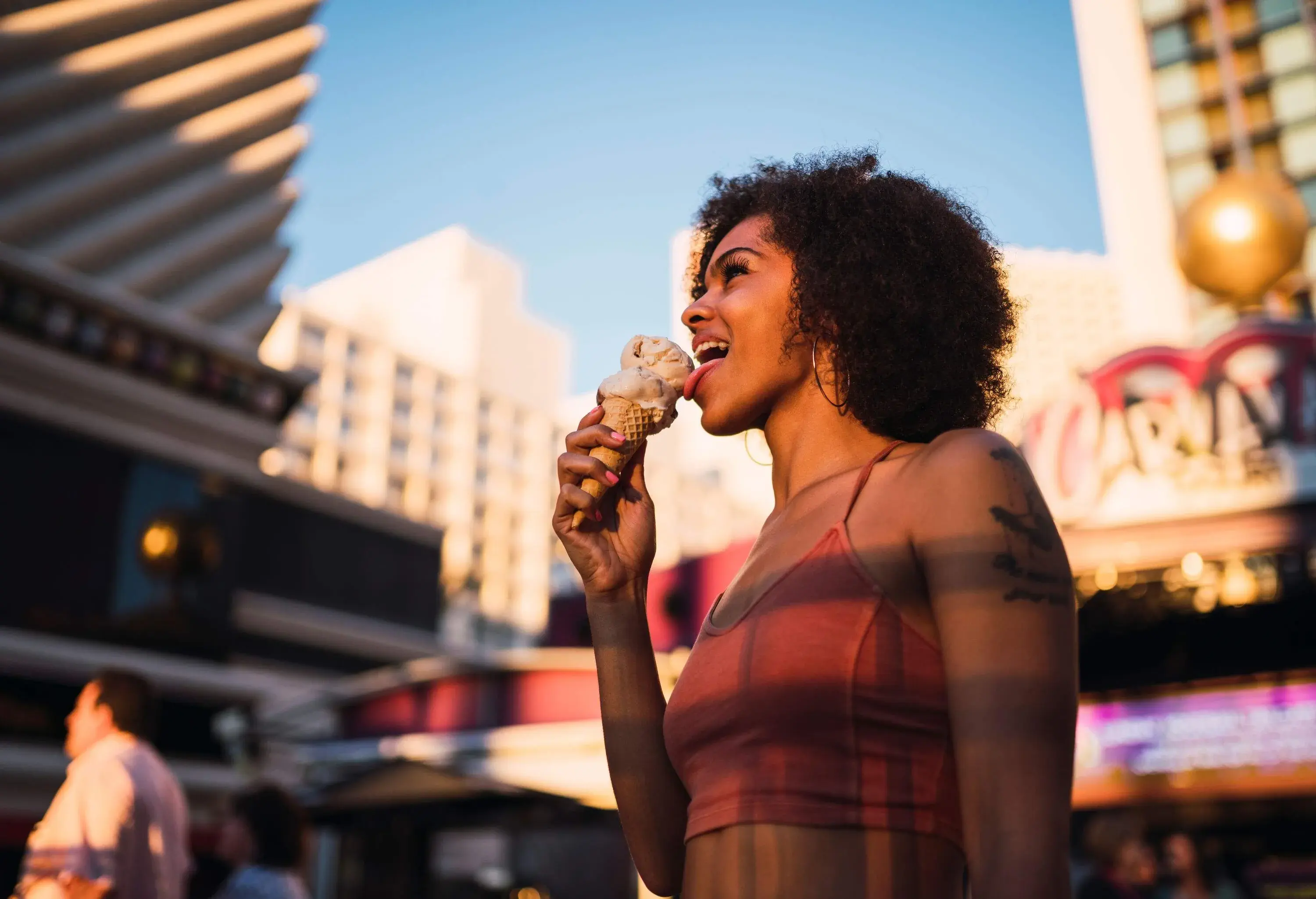 A happy woman with beautiful afro hair eating ice cream in the city.