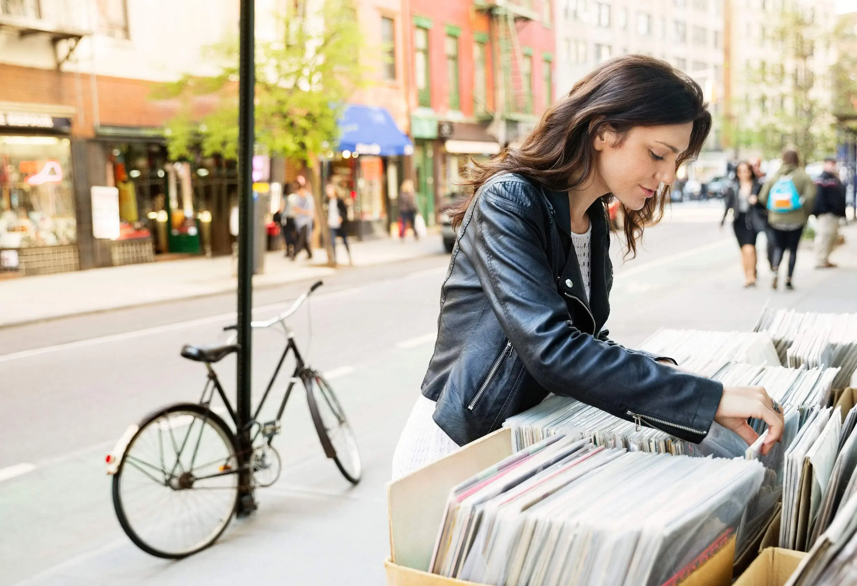 A woman browsing through boxes of magazines displayed outside of a shop.