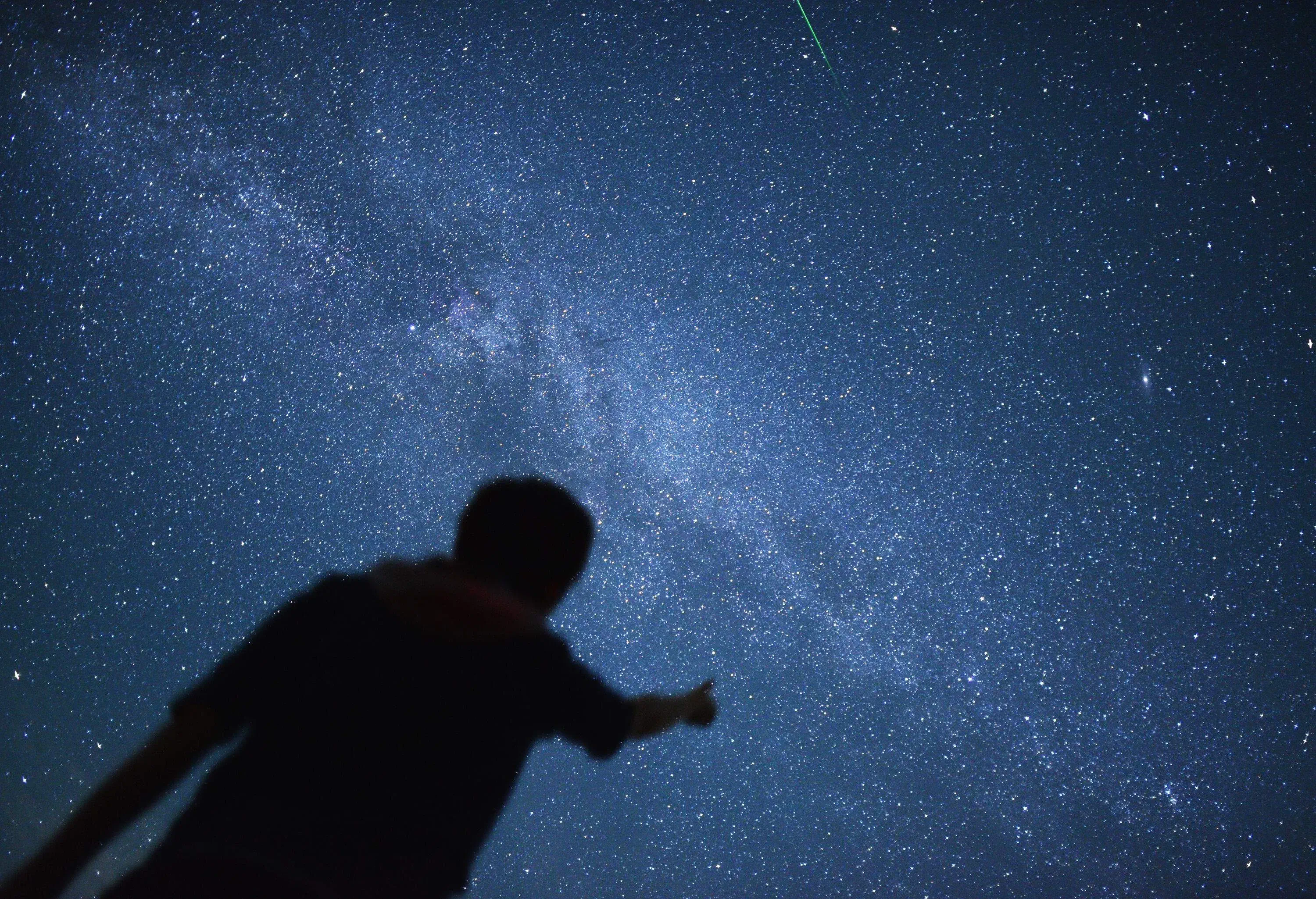 Silhouette of a person pointing at a constellation of stars.