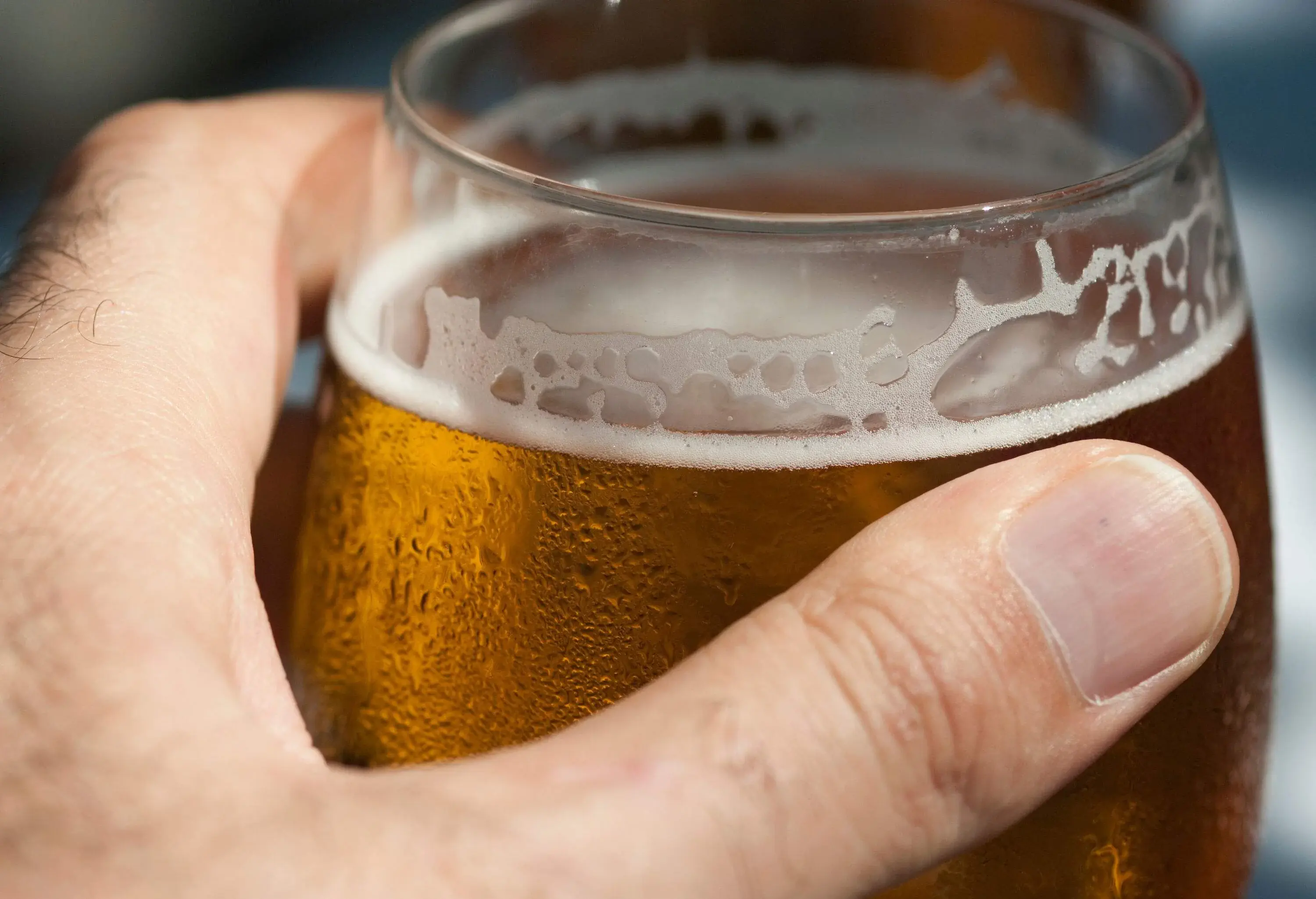 A hand holding a glass of cold beer.