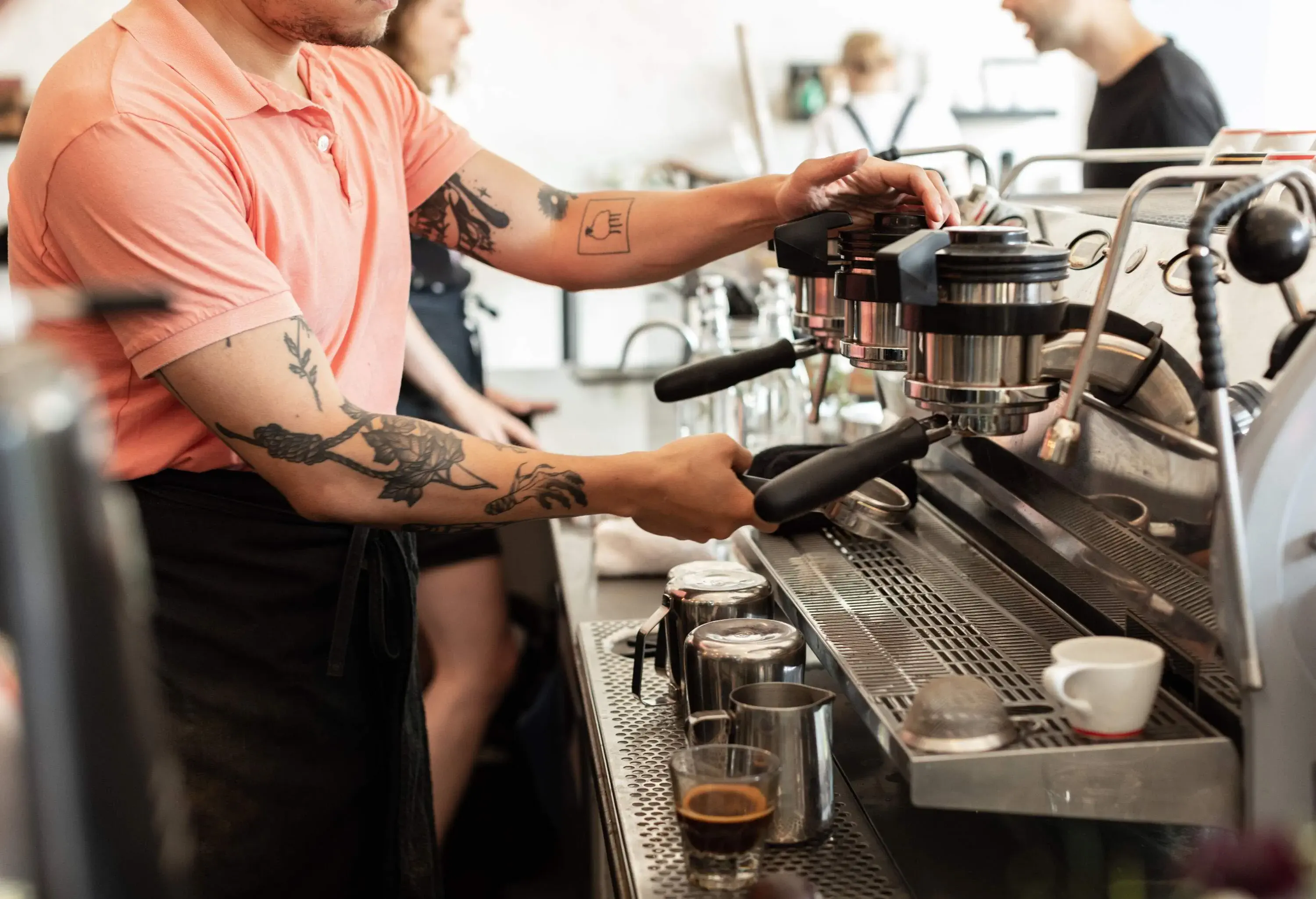 A talented barista, their tattooed arm on display, skillfully prepares a delicious cup of coffee at the espresso machine.