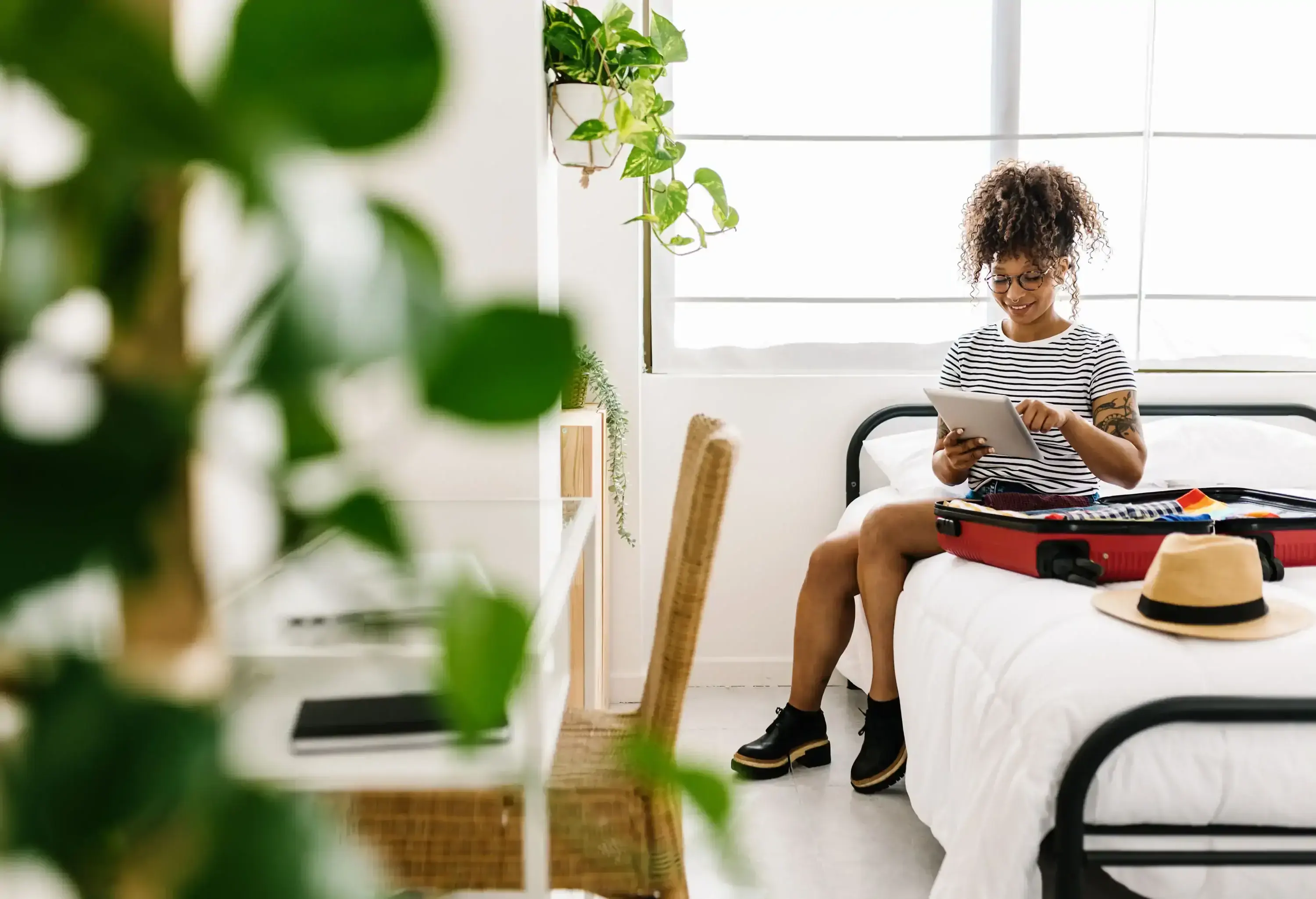 A woman sitting on the bed with her luggage, using her tablet computer.