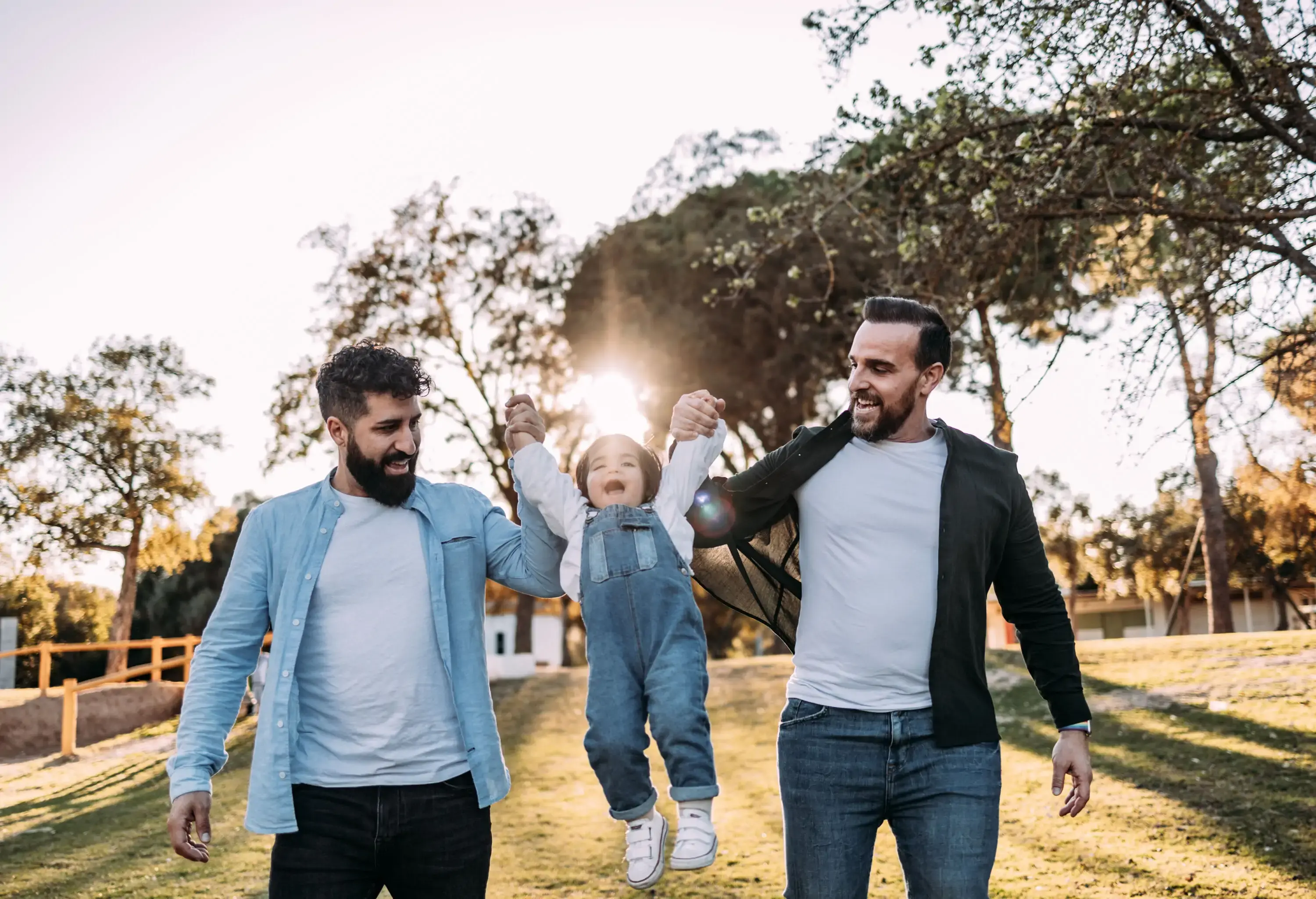 Two gay men holding a small child's hands and playfully lifting her in the air.