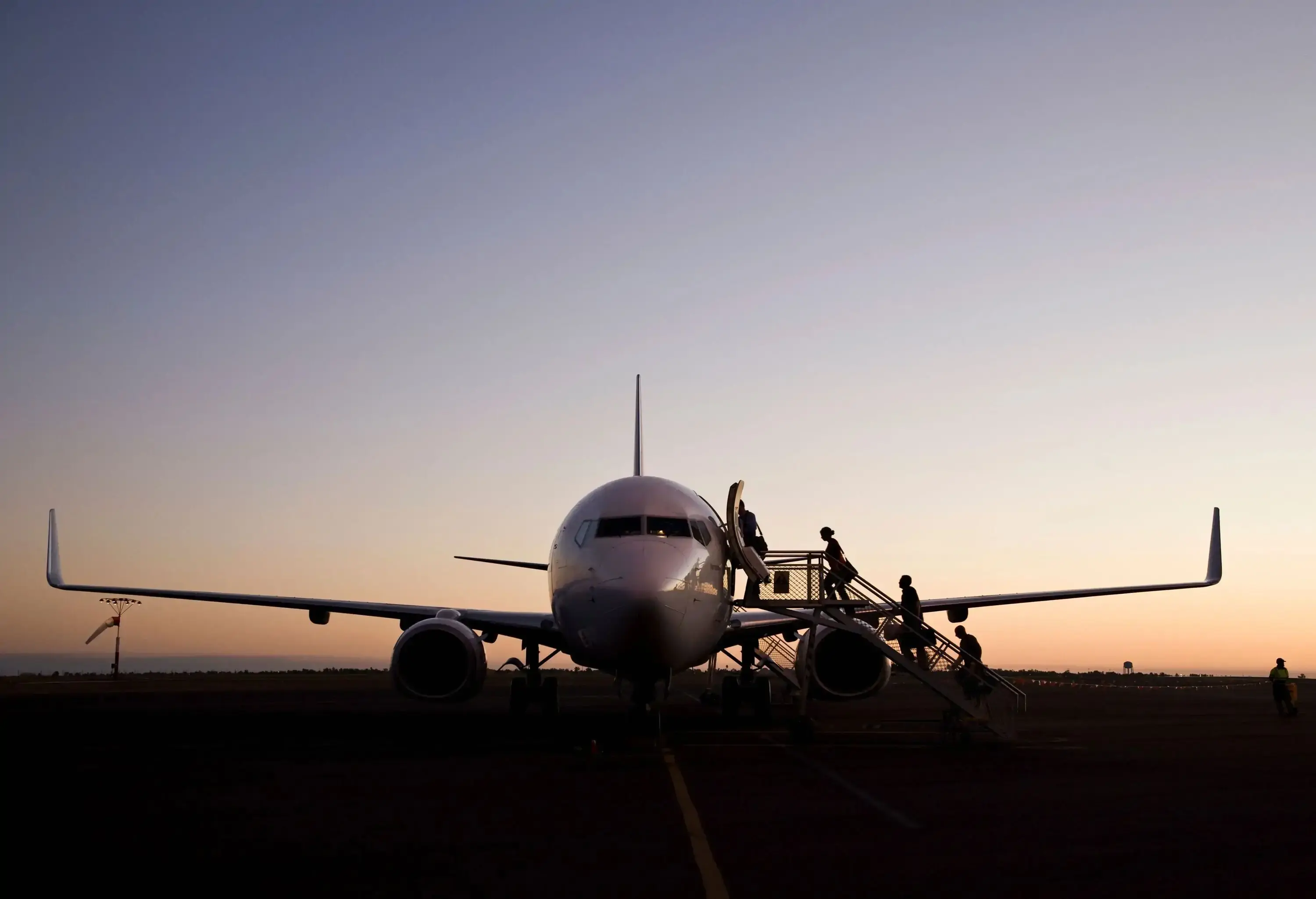 Passengers boarding an aircraft on the tarmac as the sun sets.