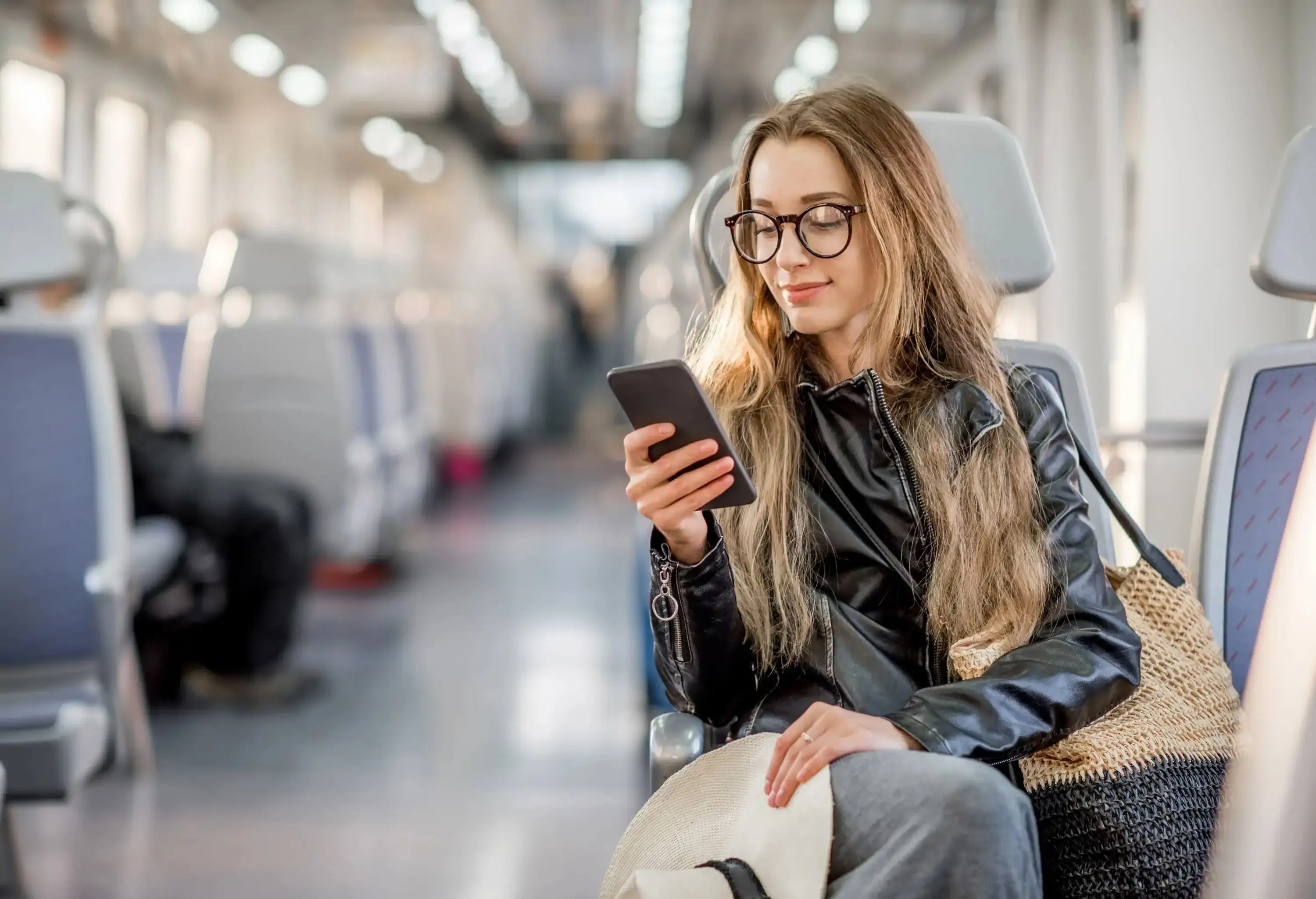 A smiling young woman sits inside public transportation while using her mobile phone.
