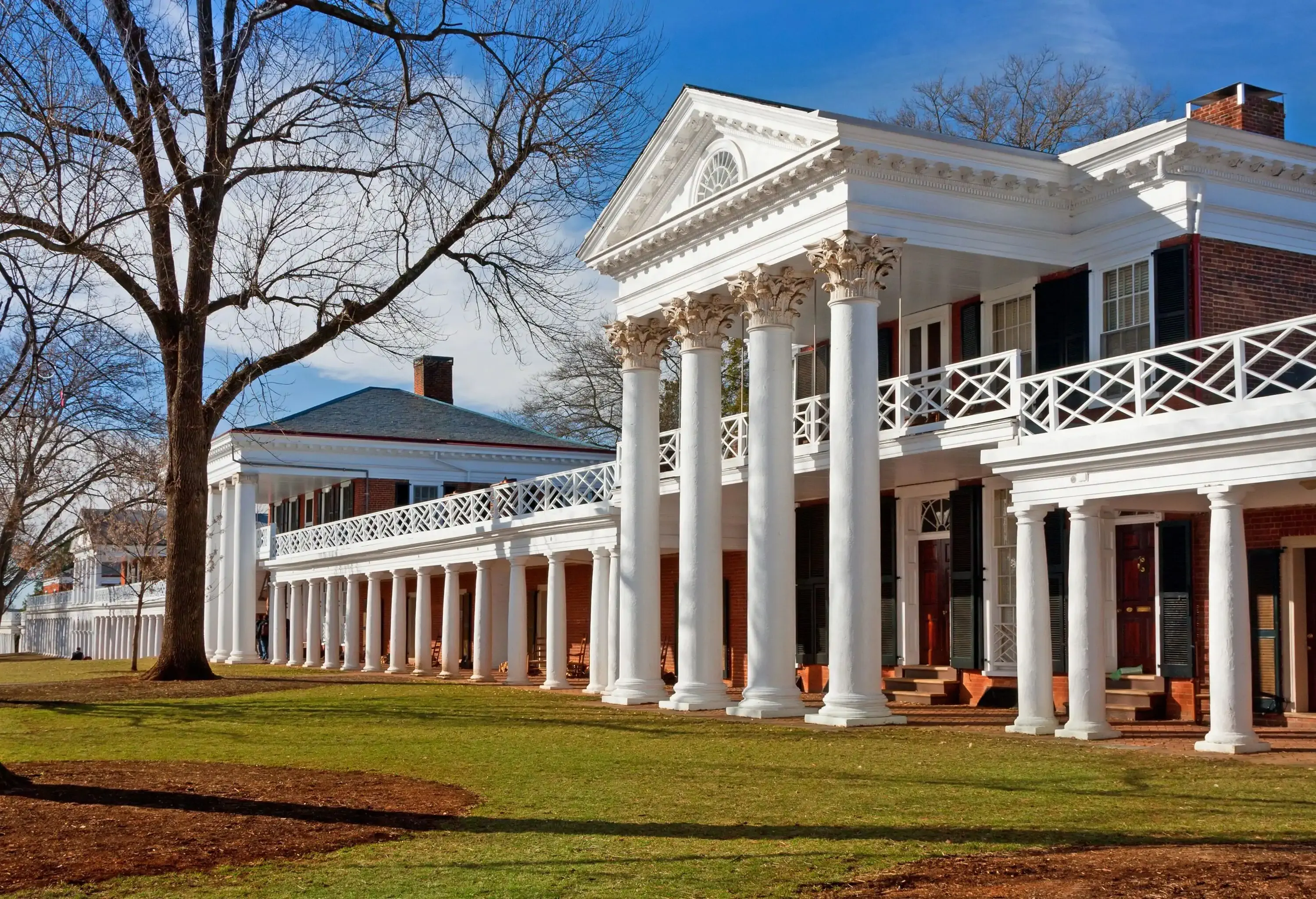 A Roman style building with a tetrastyle portico and a freestanding colonnade along a covered walkway painted in white.