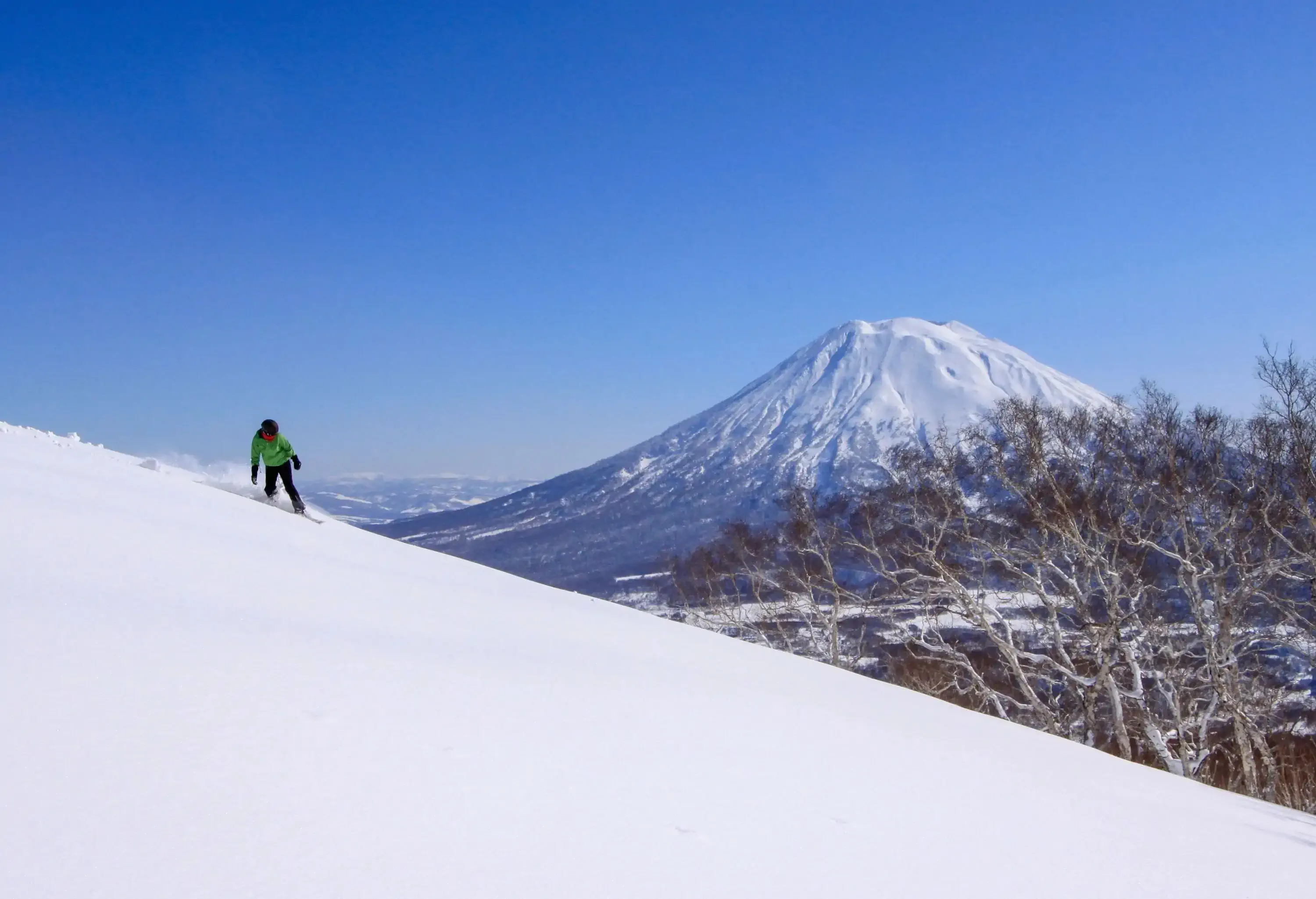Skier on a slope overlooking a volcanic mountain covered in snow on a sunny day in winter