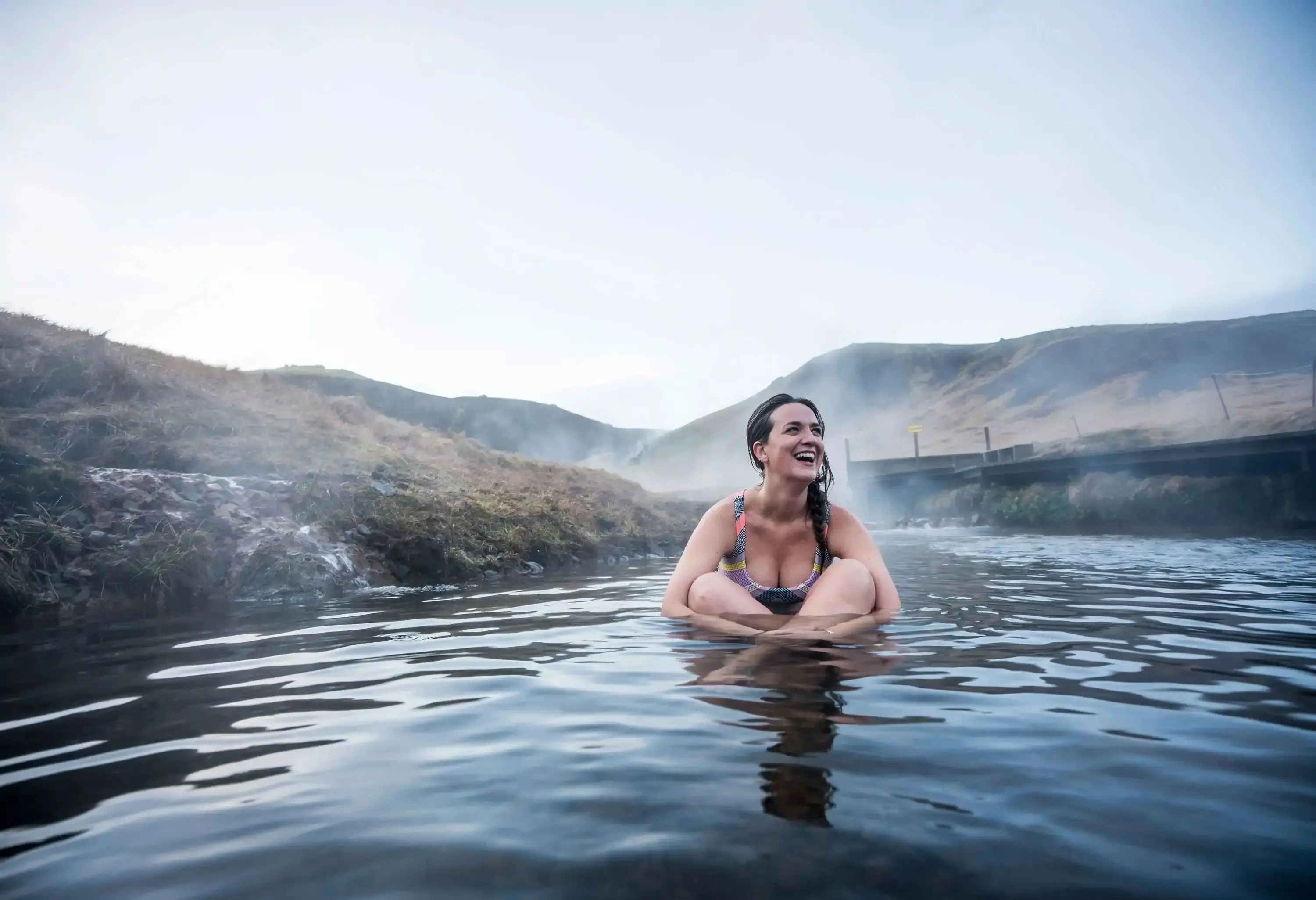 Smiling woman sitting in natural hot spring surrounded by hills