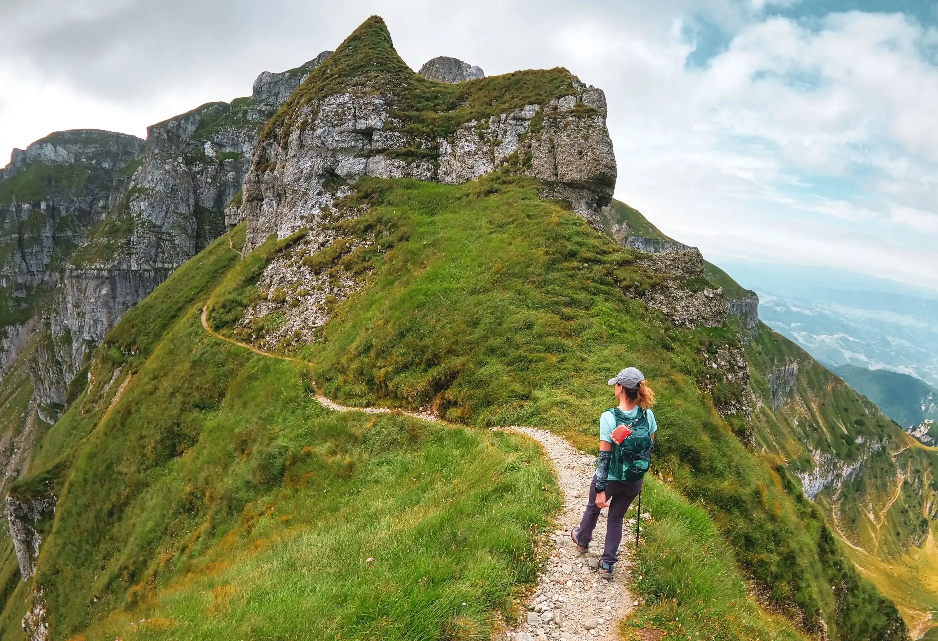 panoramic views over the glacial valleys and woman hiking trail on a cloudy day