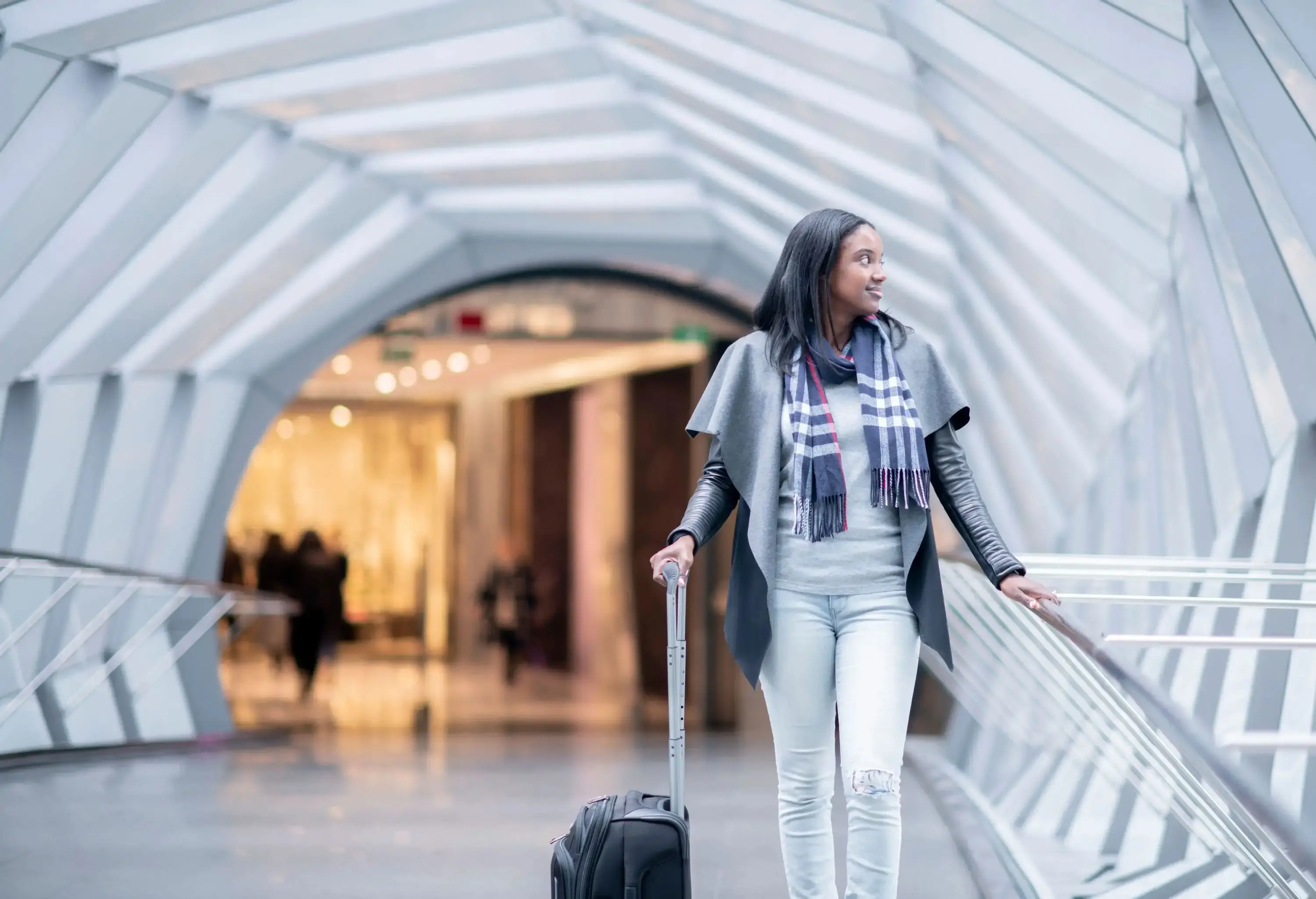 A woman of African descent is walking through an airport. She is carrying a suitcase and looking around.