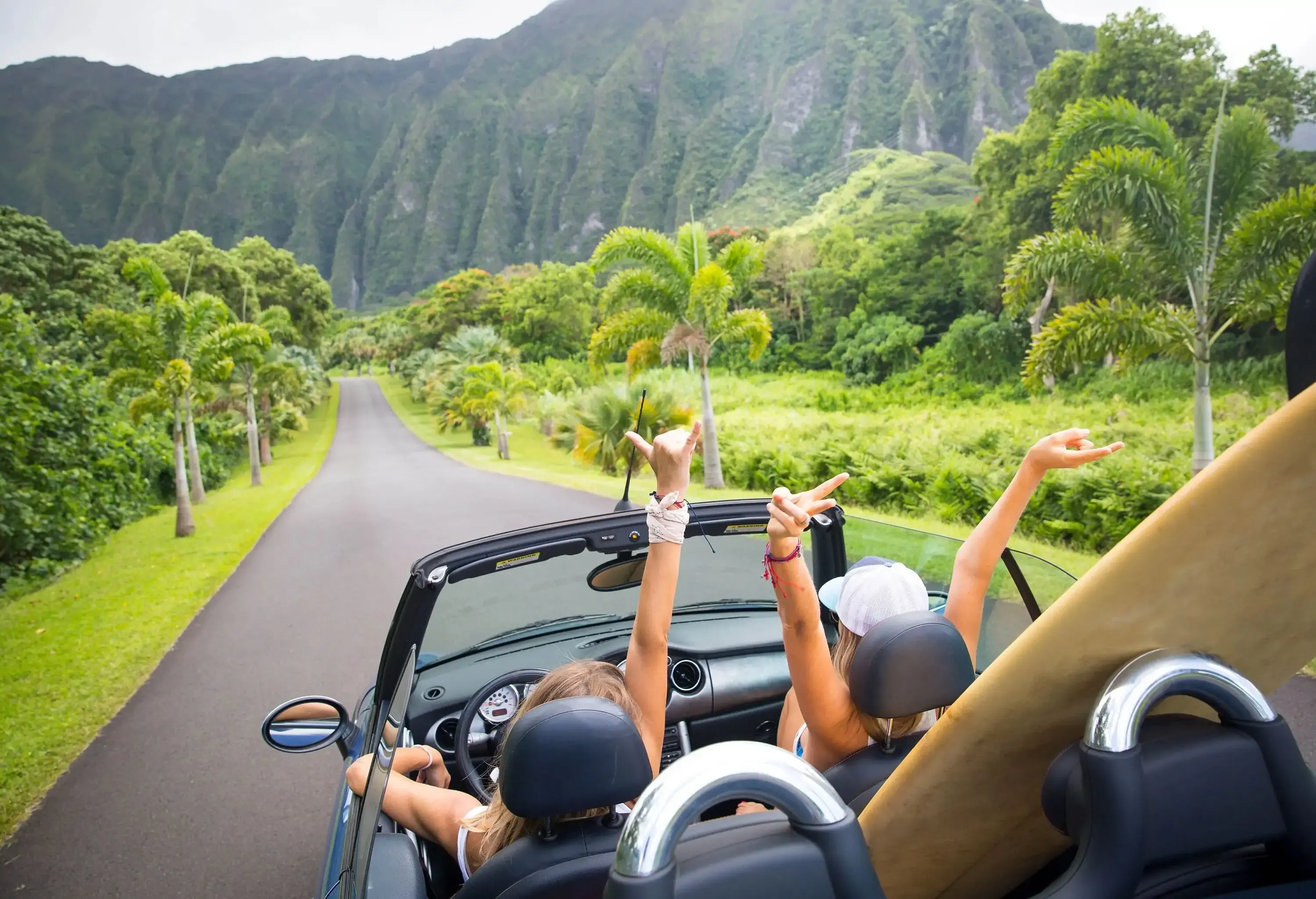 Road trip travel - girls driving car in freedom. Happy young girls cheering in convertible car on summer Hawaii vacations.