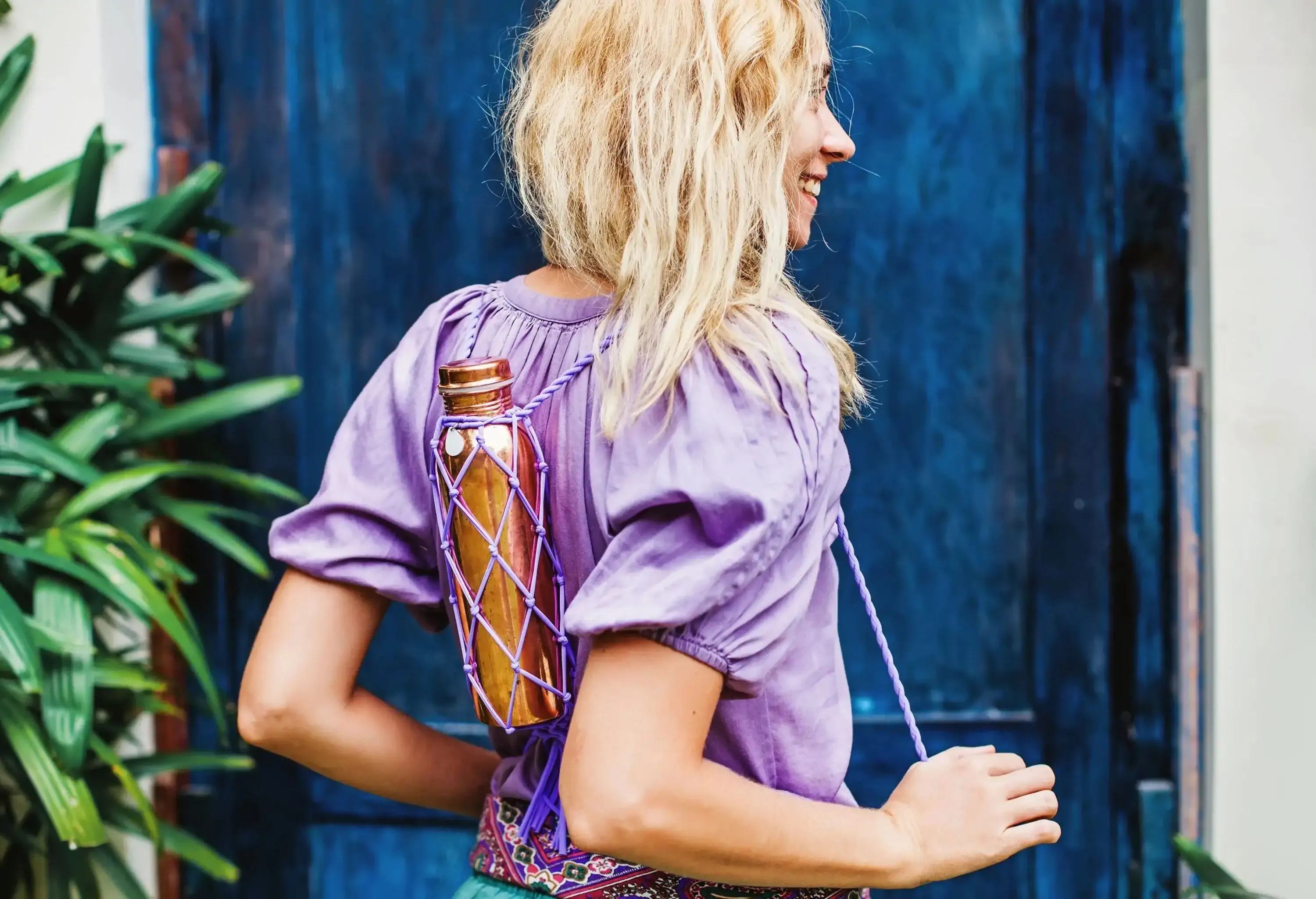 A blonde woman wears a knitted handle with a reusable copper water bottle.