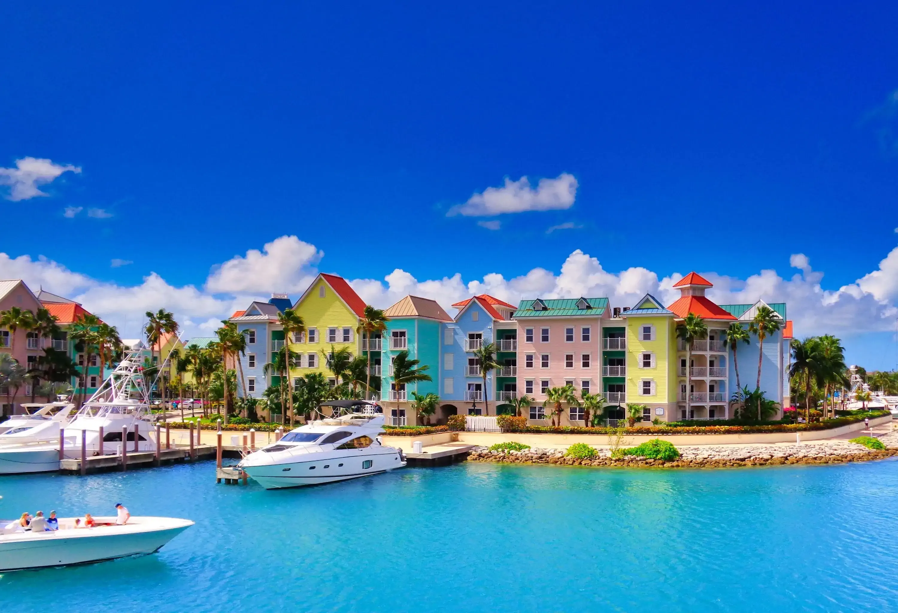 Colourful houses with moored yachts on the shore of the turquoise sea against the cloudy blue sky.
