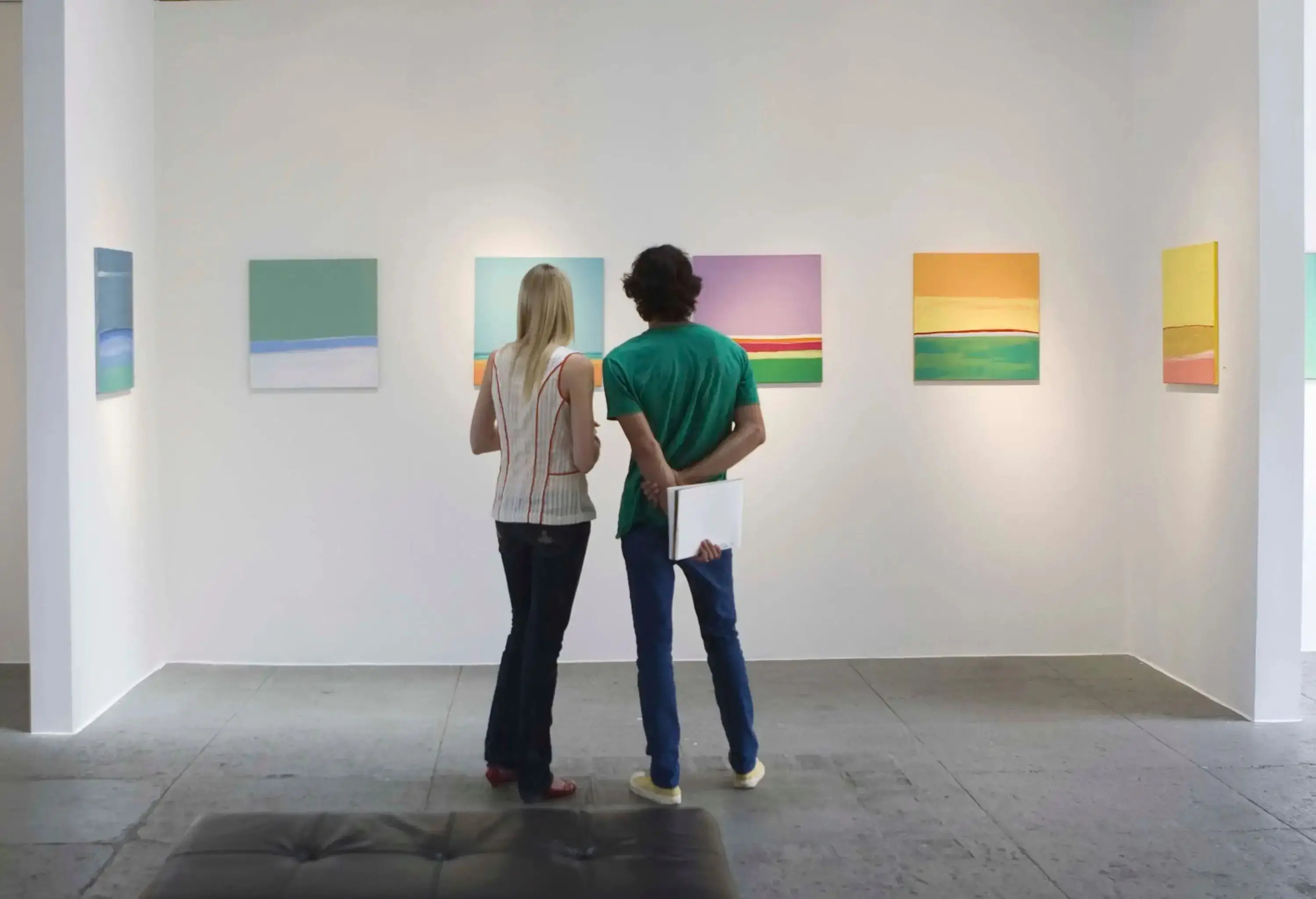 A male and a female friend are looking at the paintings in the museum.