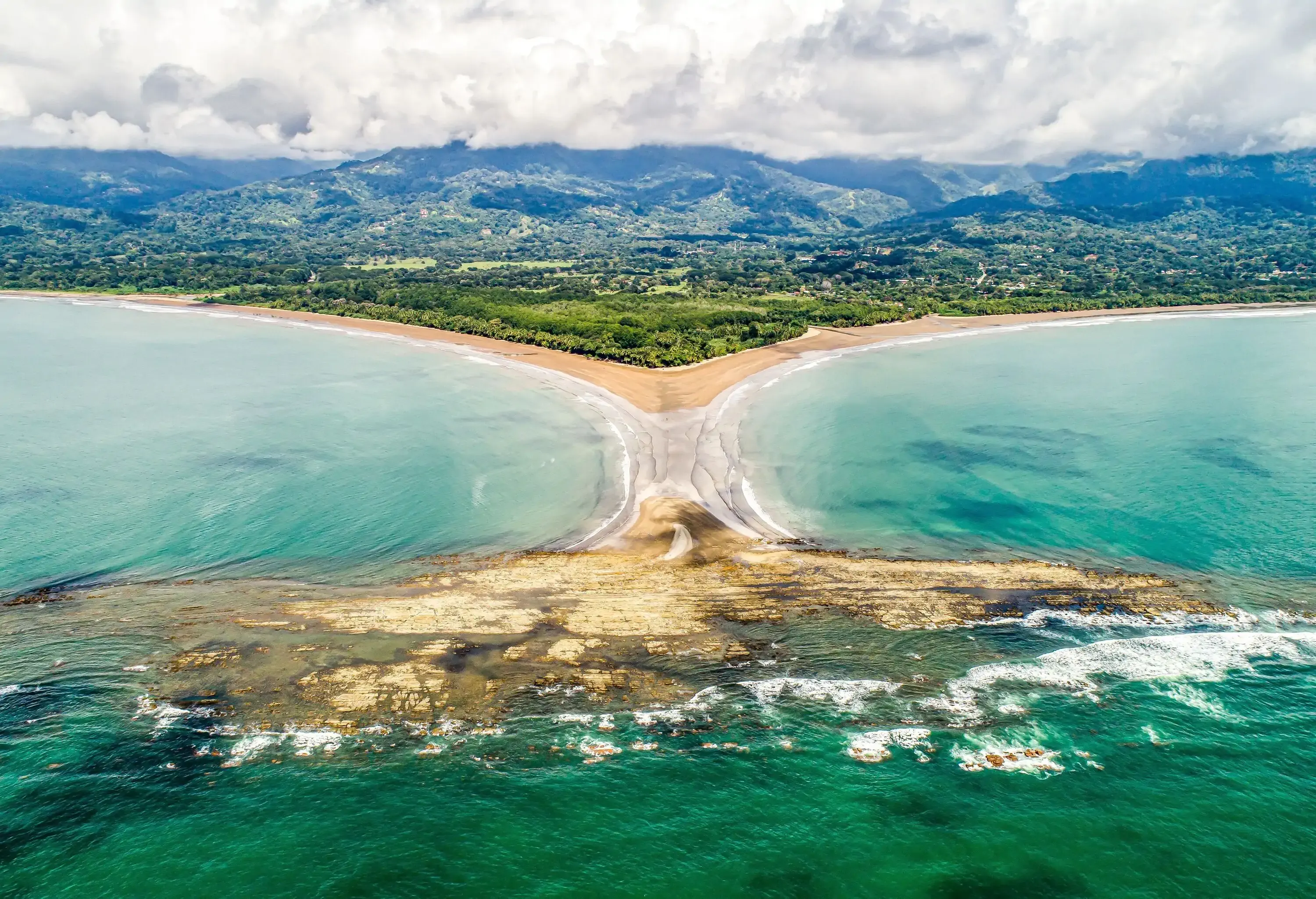 The beautiful beach of Costa Rica's Pacific coast unfurls in the shape of a whale tail where the tropical forest meets the sandy shores, creating a unique and stunning coastal landscape.