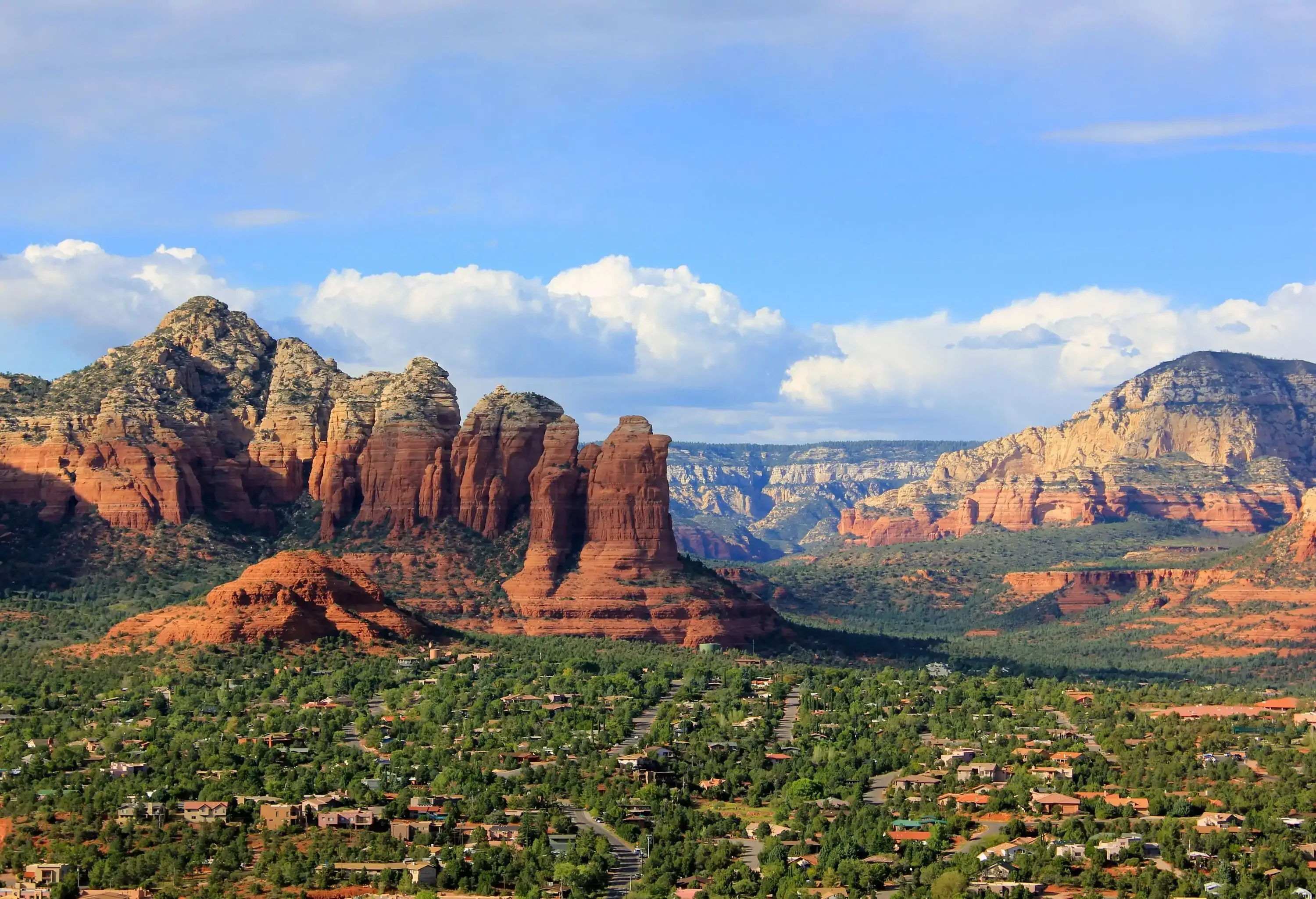 Houses scattered on the flatland in lush evergreen vegetation against a red rock scenery backdrop.