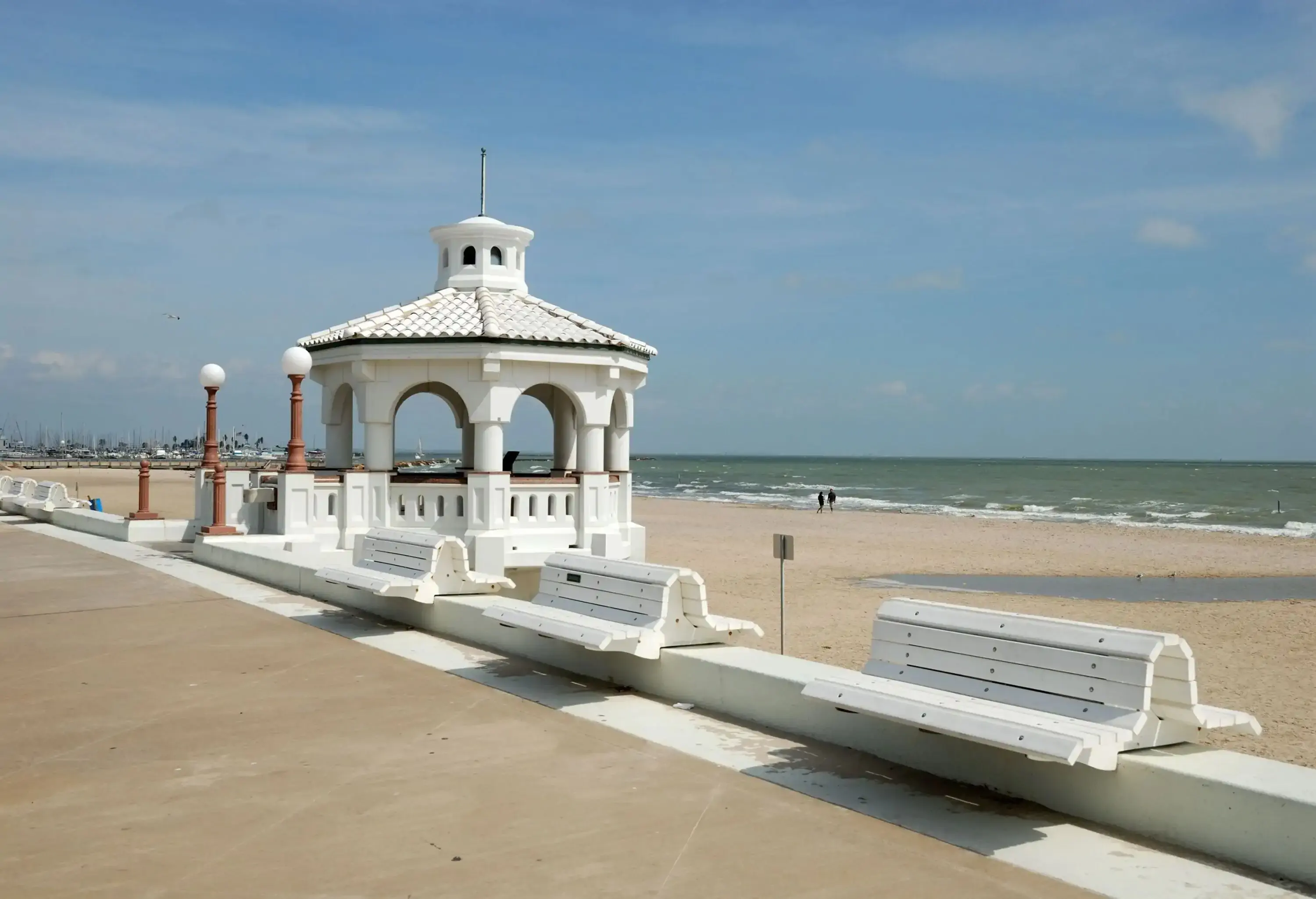 A promenade along a beach with a white pavilion lined with white benches.