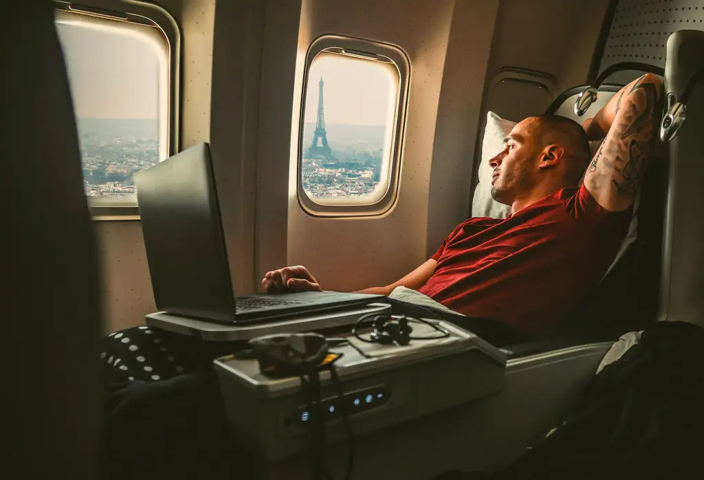 Man relaxing in airplane seat with Eiffel Tower visible through the window.