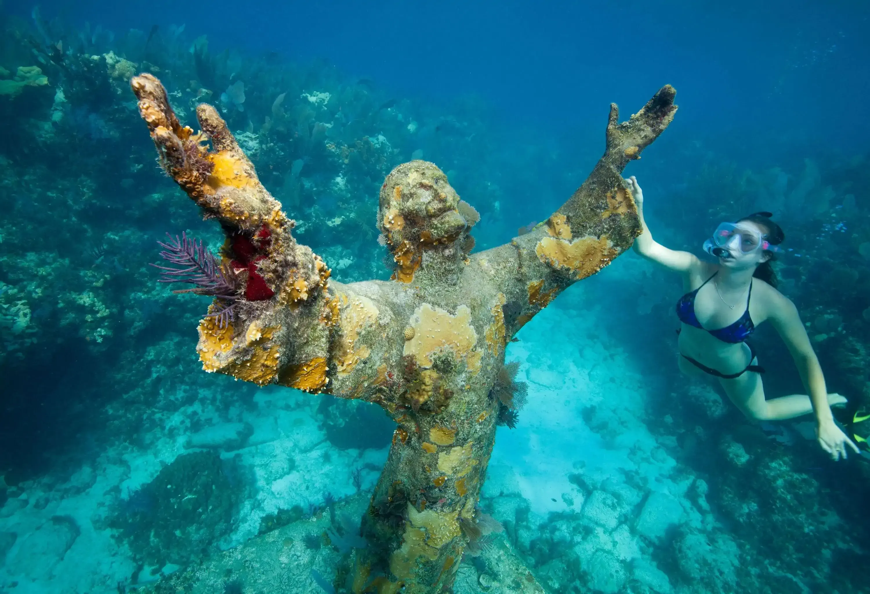 A young woman swimming around the submerged Christ of the Abyss statue.