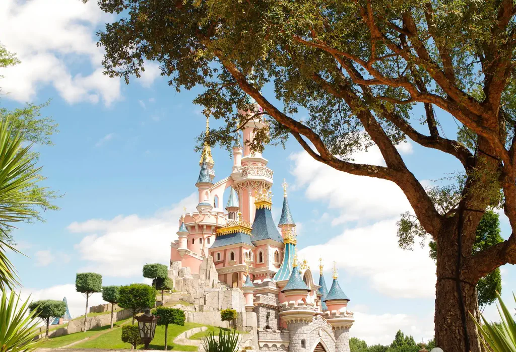 Sleeping Beauty Castle at Disneyland Paris framed by trees under a bright blue sky.