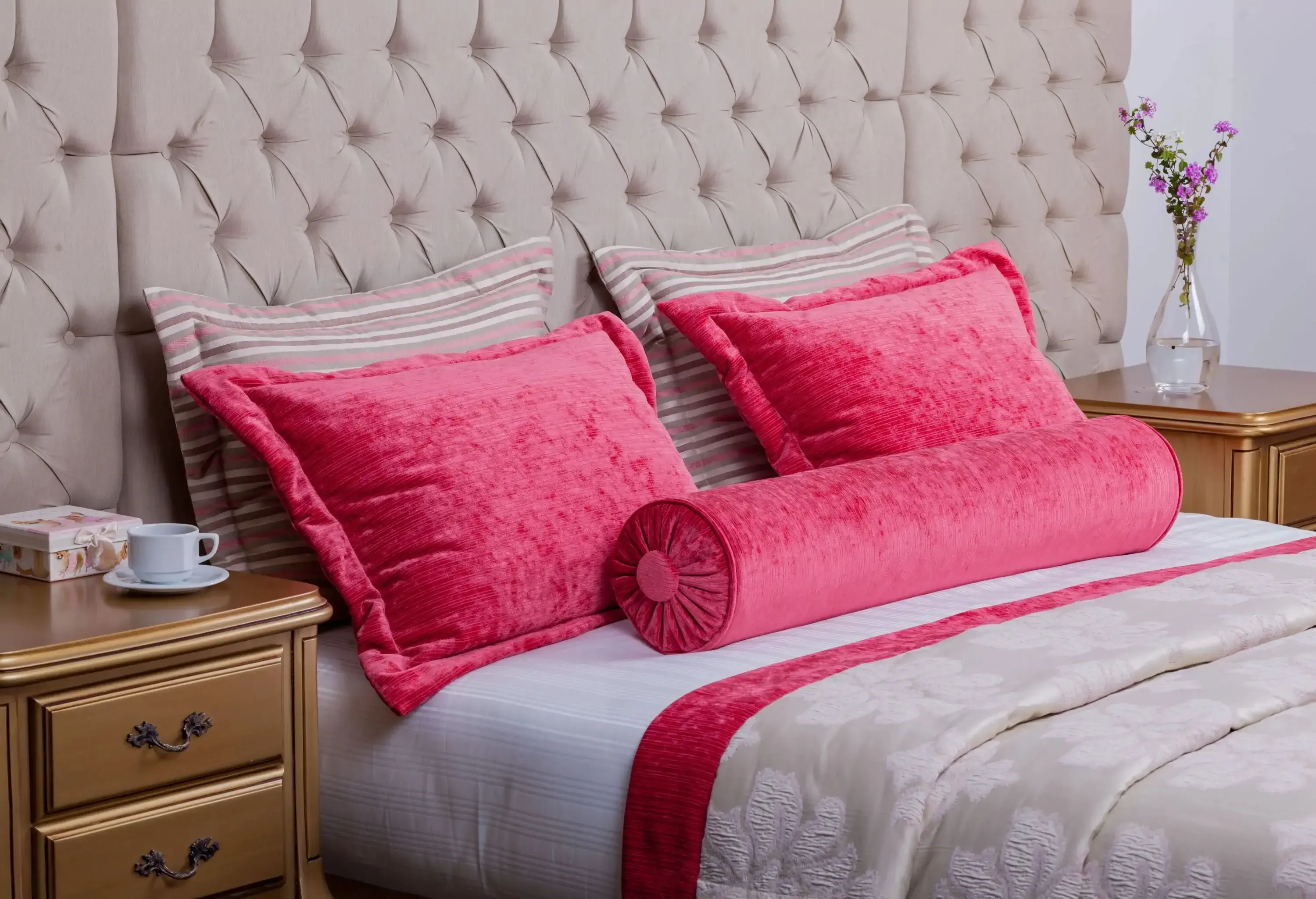 A pair of cherry velvet and another pair of pink pillows lean against a tufted headboard in a cosy room.