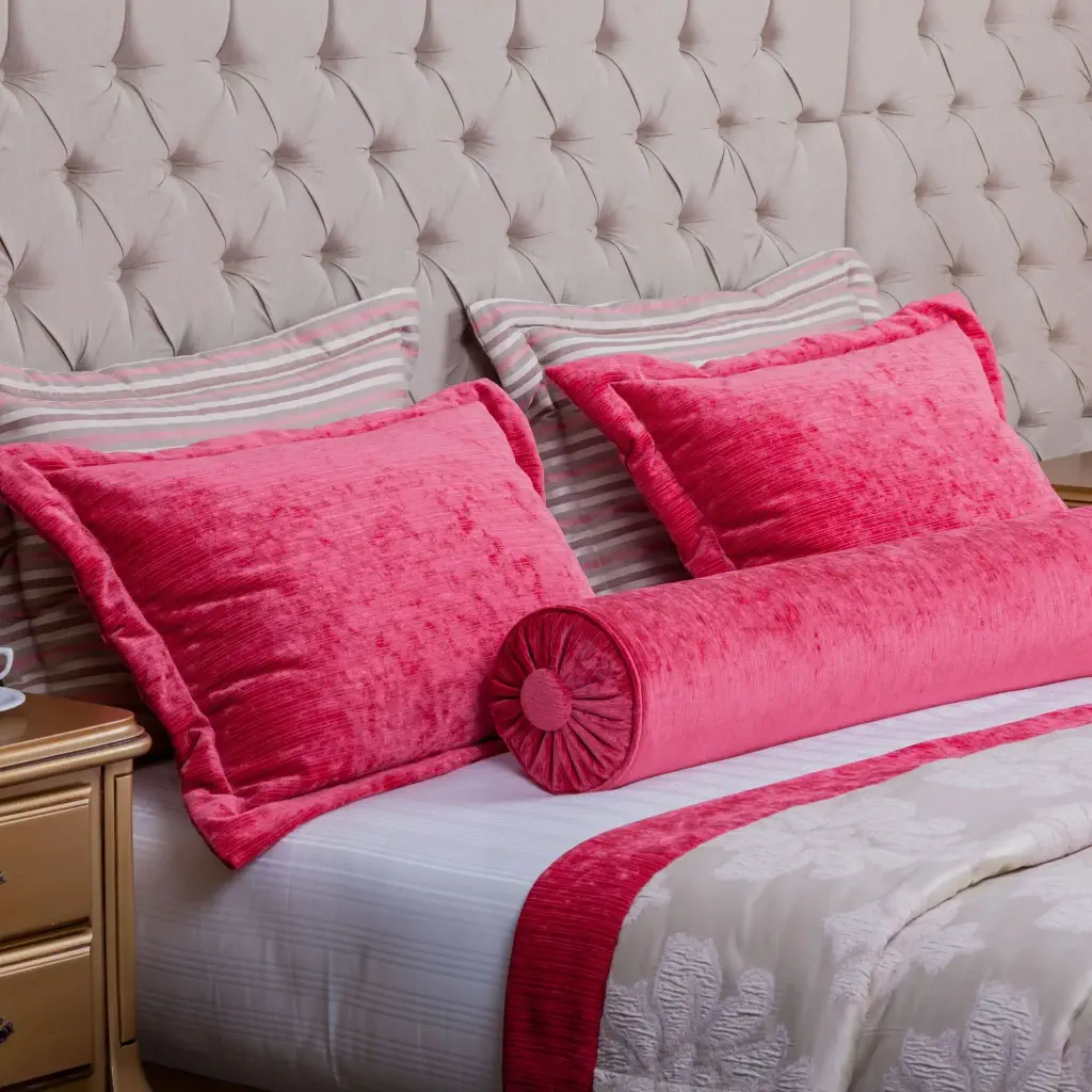 A pair of cherry velvet and another pair of pink pillows lean against a tufted headboard in a cosy room.