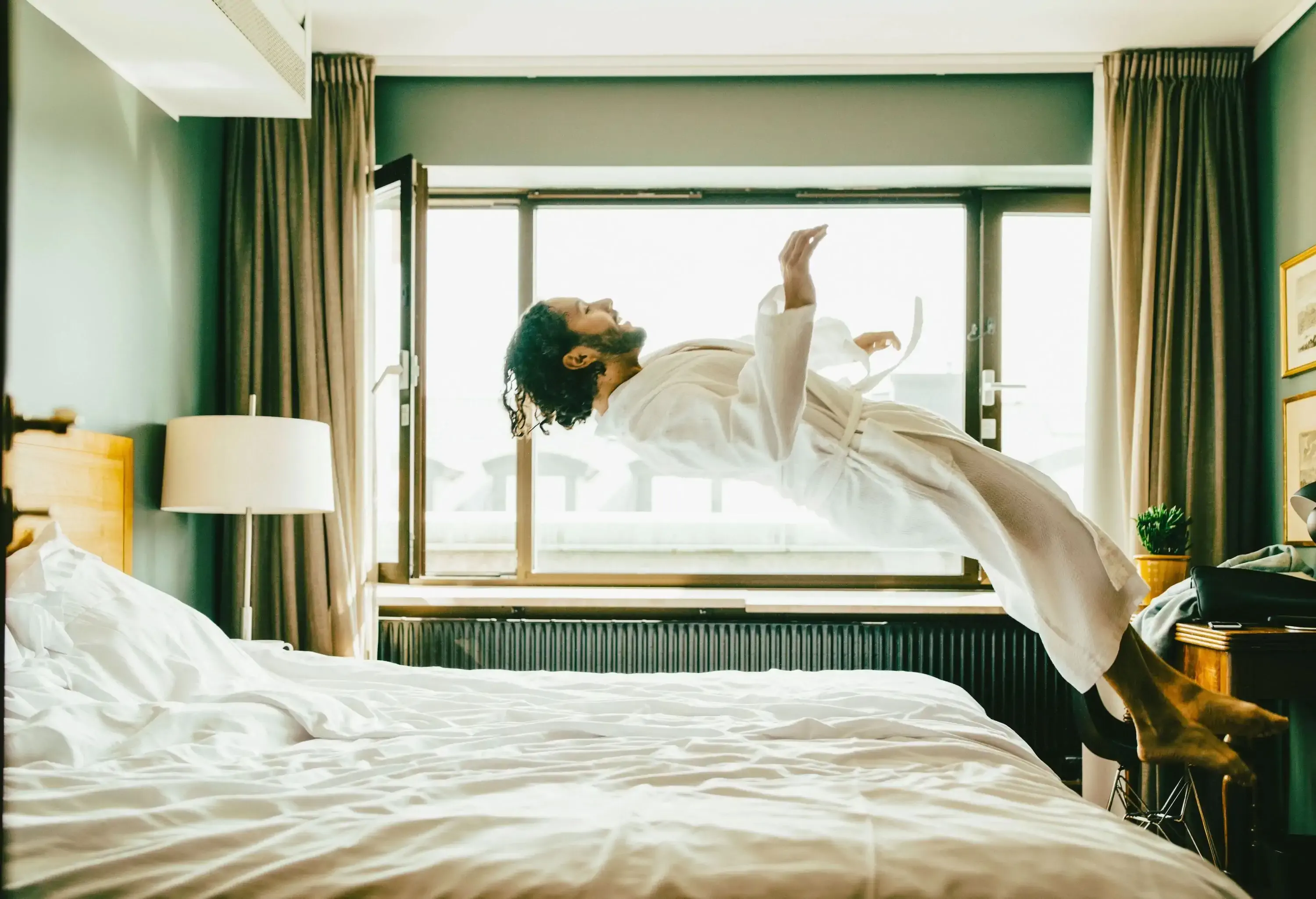 man wearing robe jumping into hotel room bed