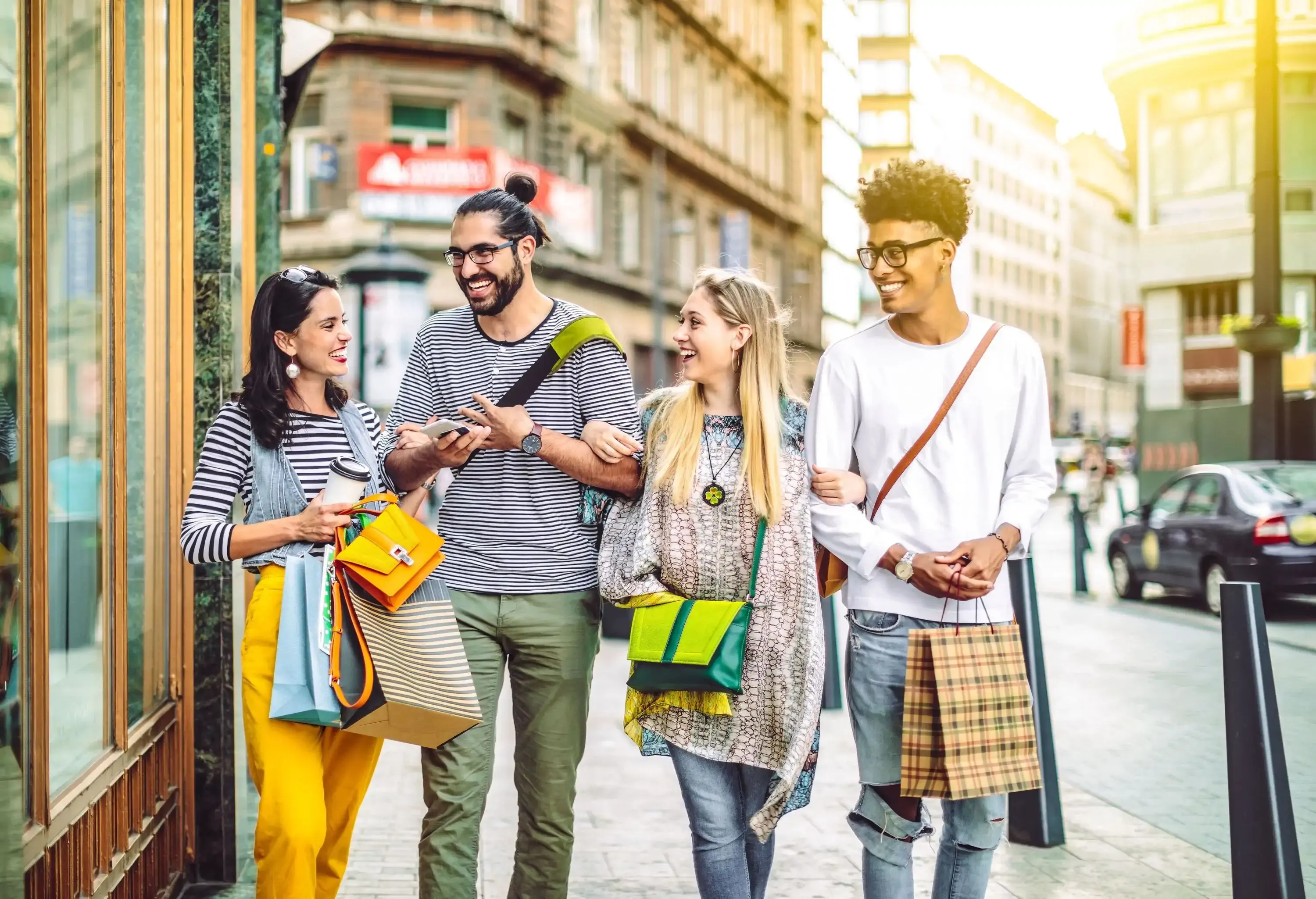A group of four people happily smiling while holding shopping bags as they walk along a street.