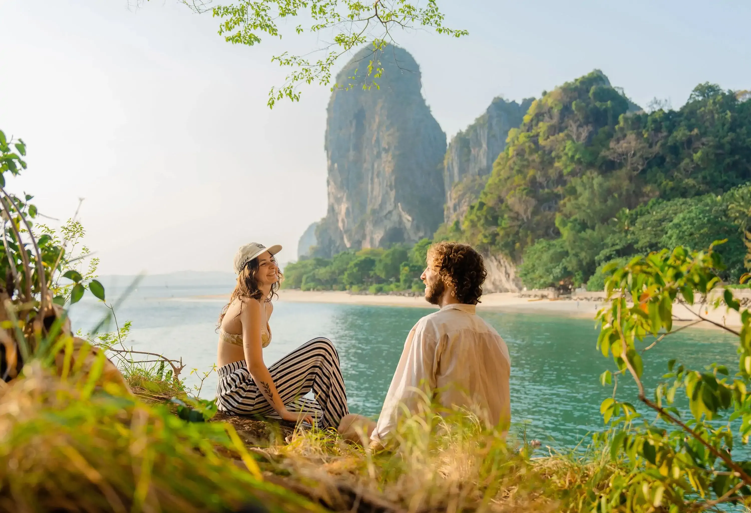 Young woman and man  sitting  and talking on cliff  on the background of  Railey  bay
