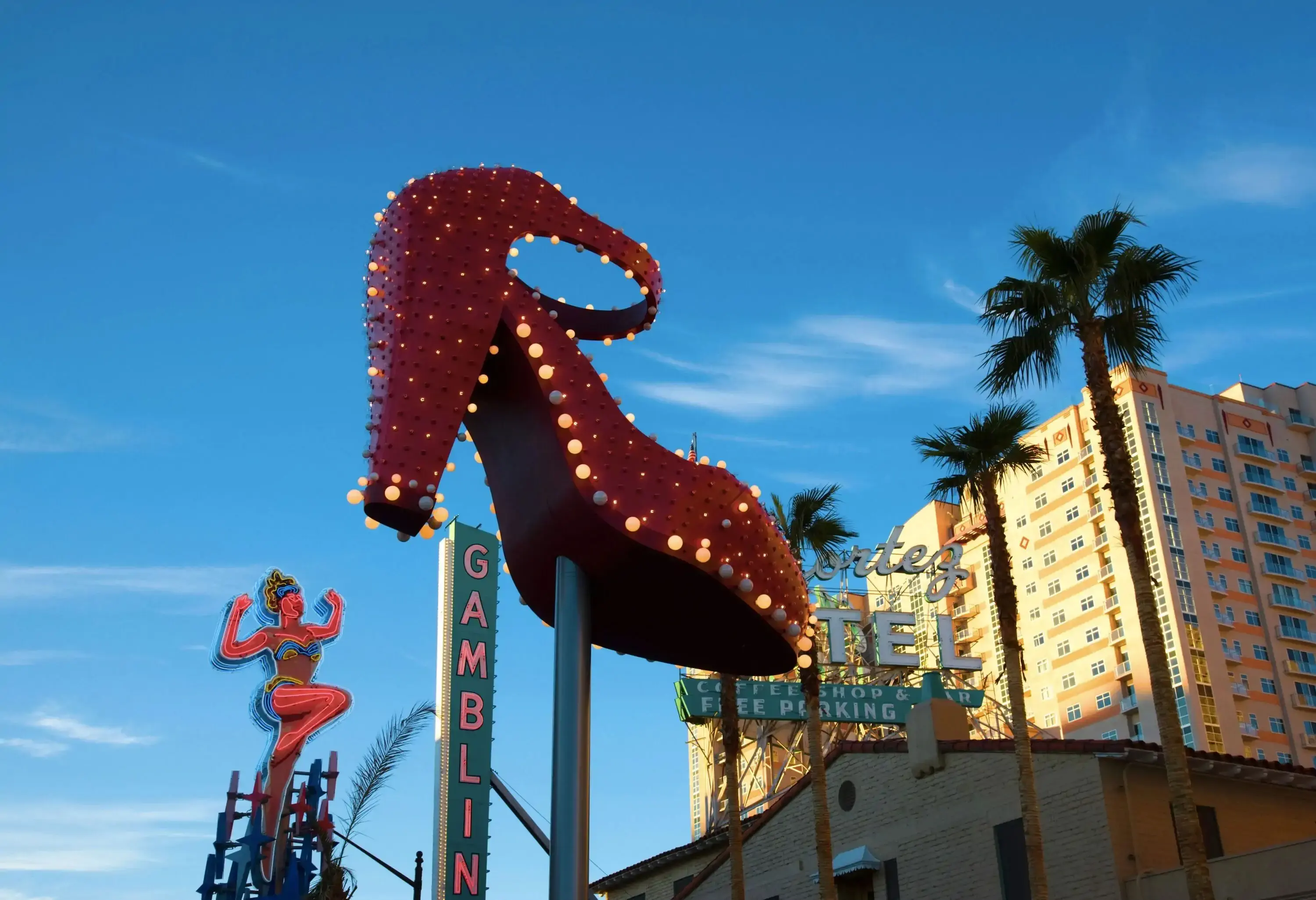 A huge red shoe with lighted bulbs, a showgirl, and gambling signage protrudes toward the clear blue sky.
