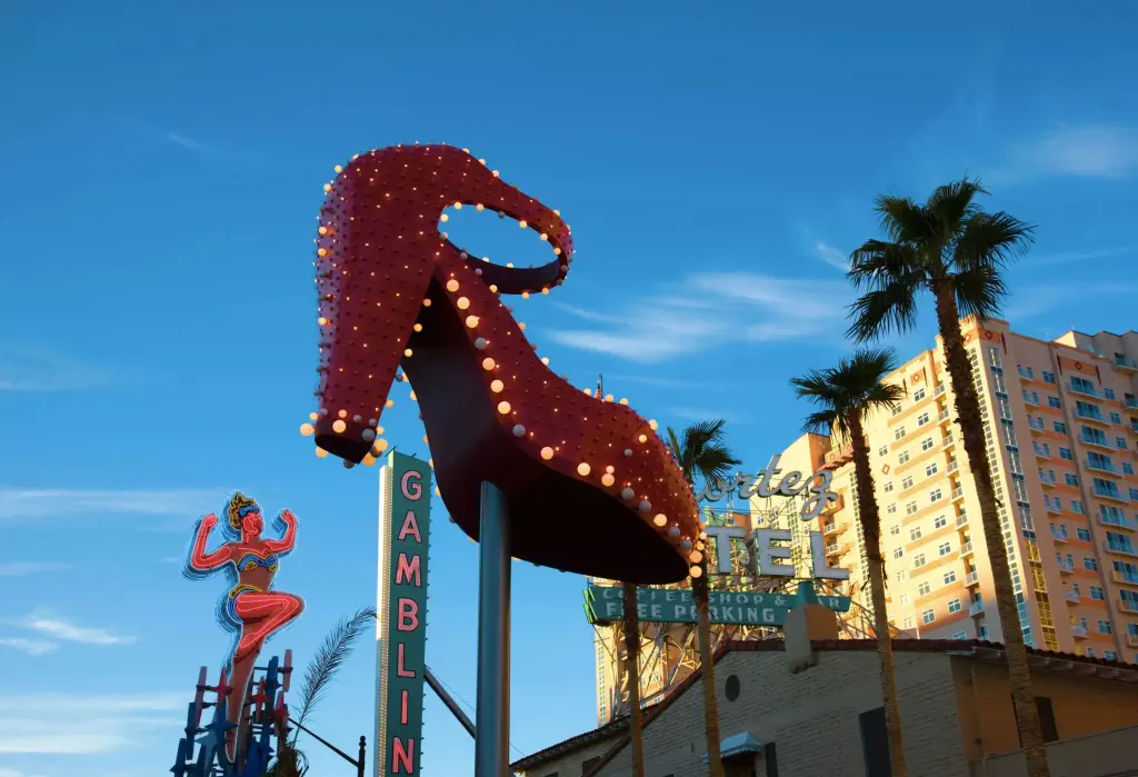 A huge red shoe with lighted bulbs, a showgirl, and gambling signage protrudes toward the clear blue sky.