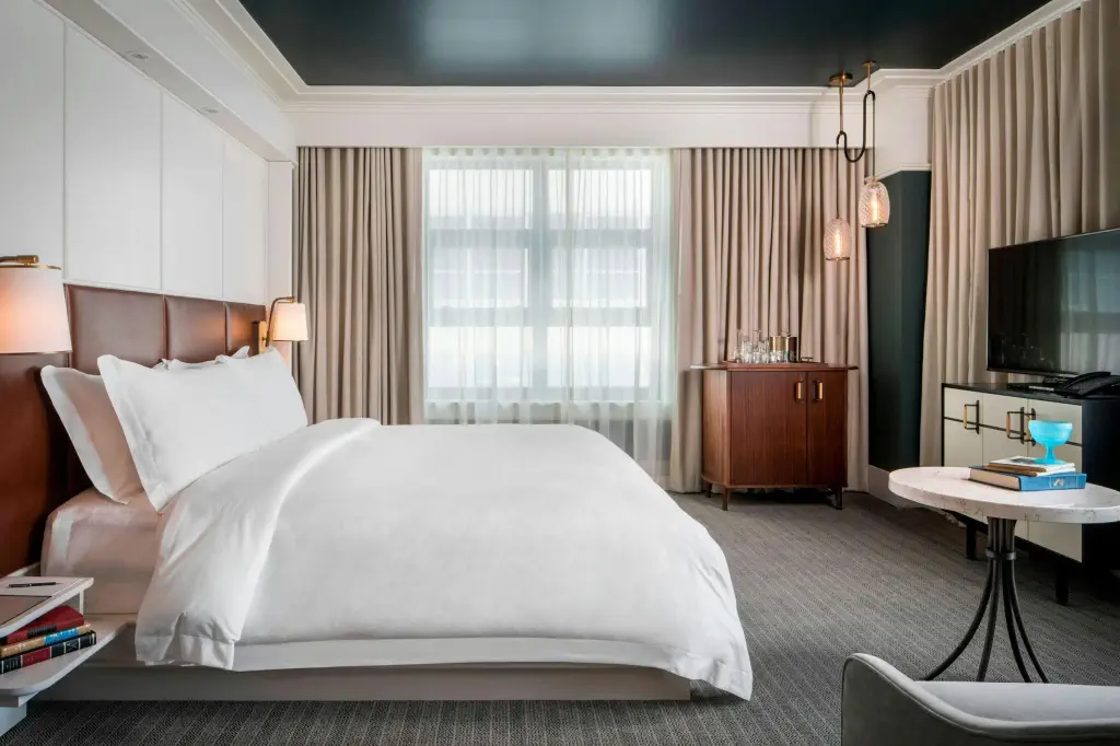 Elegant hotel room with a large white bed, modern lamps, and neutral curtains.