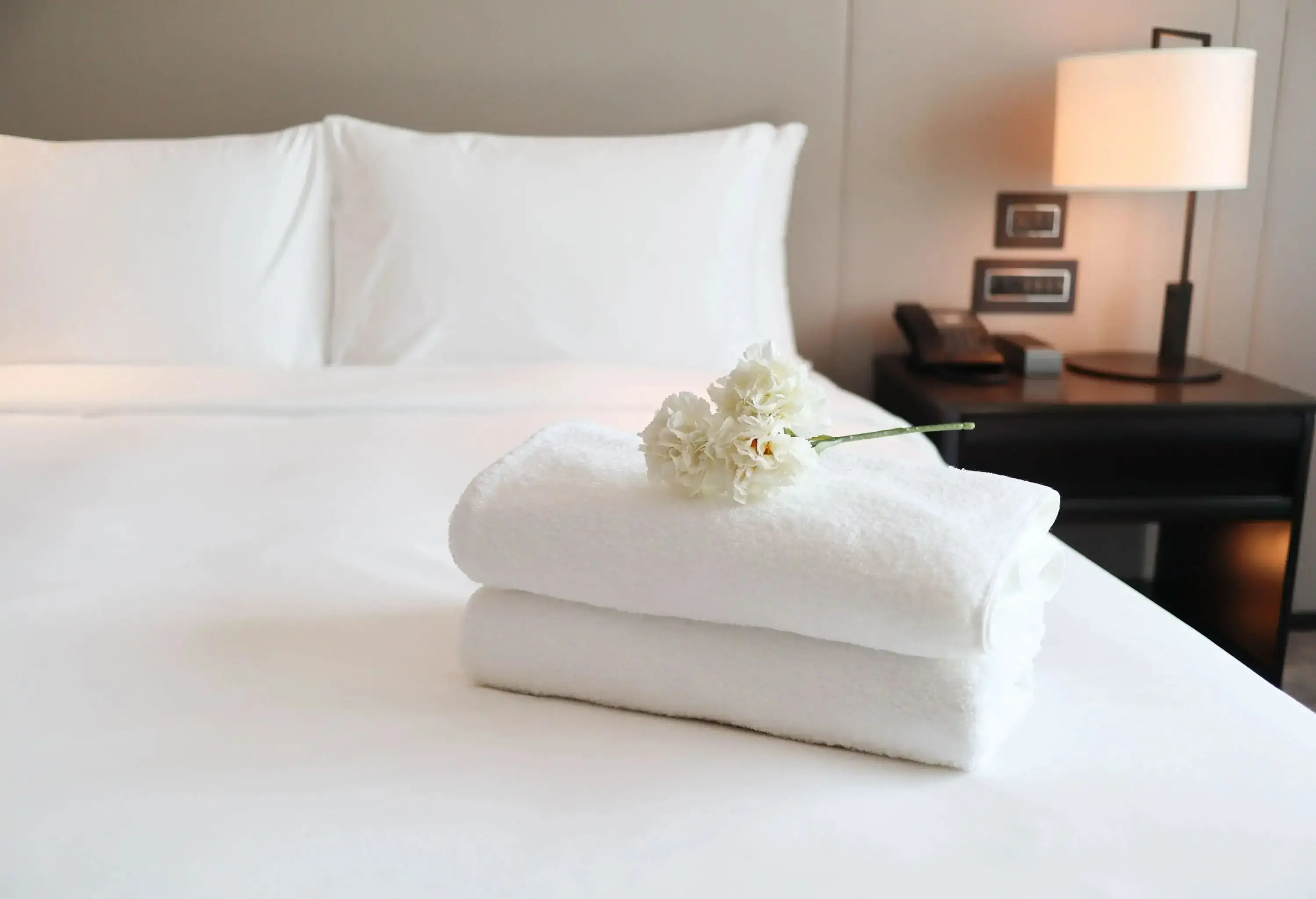 two perfectly folded towels with a flower placed on top on a hotel bed