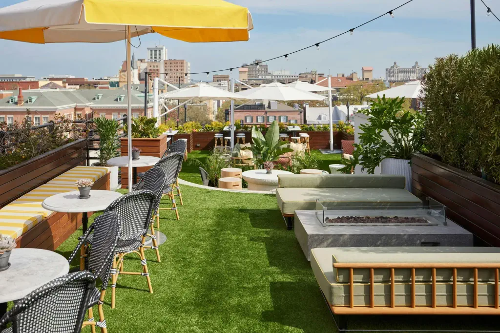 Rooftop patio with green artificial grass, yellow-striped benches, and modern chairs around small tables. 