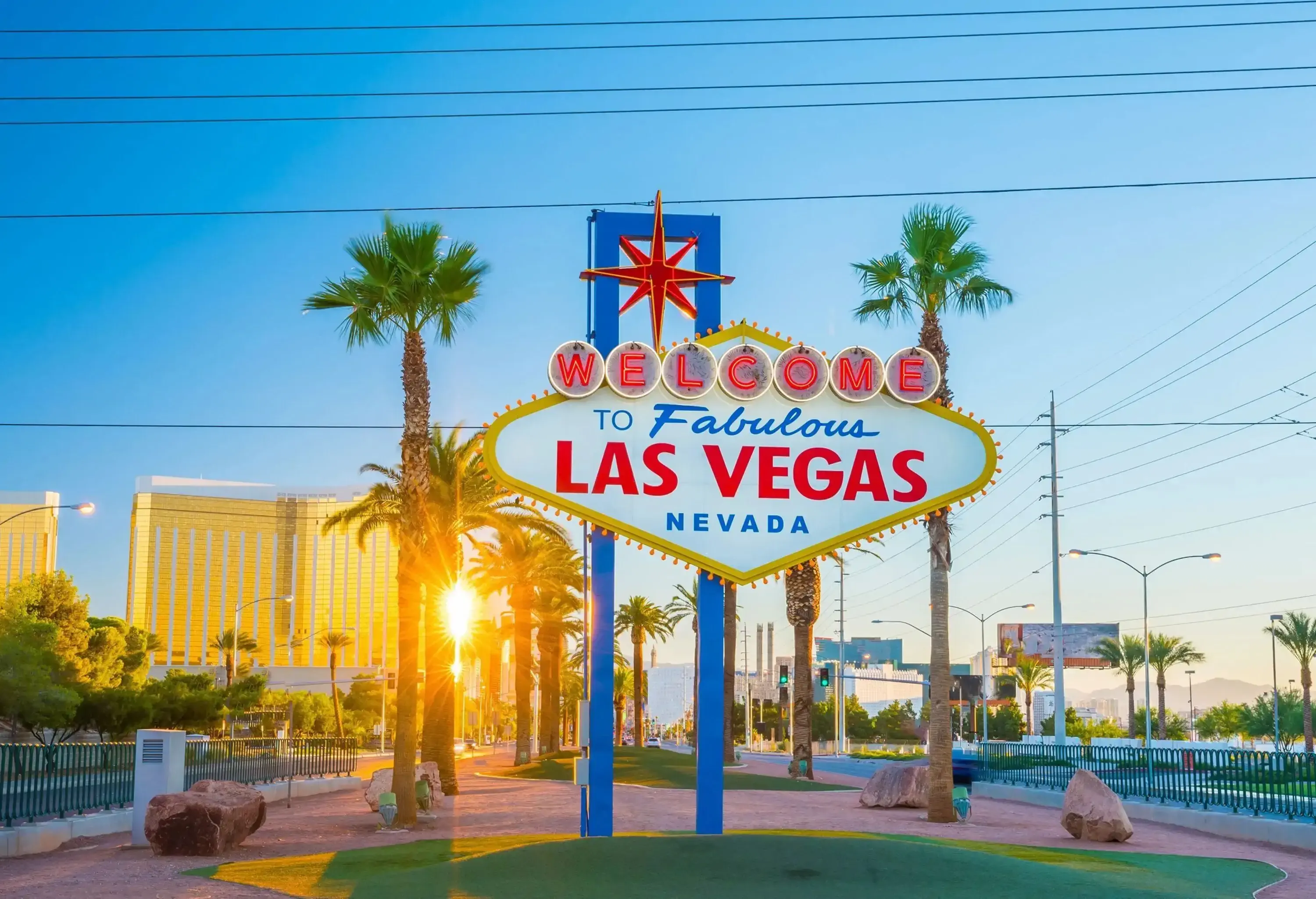 The well-known Las Vegas roadside sign, with sunlight beaming through the trunks of palm trees in the backdrop.