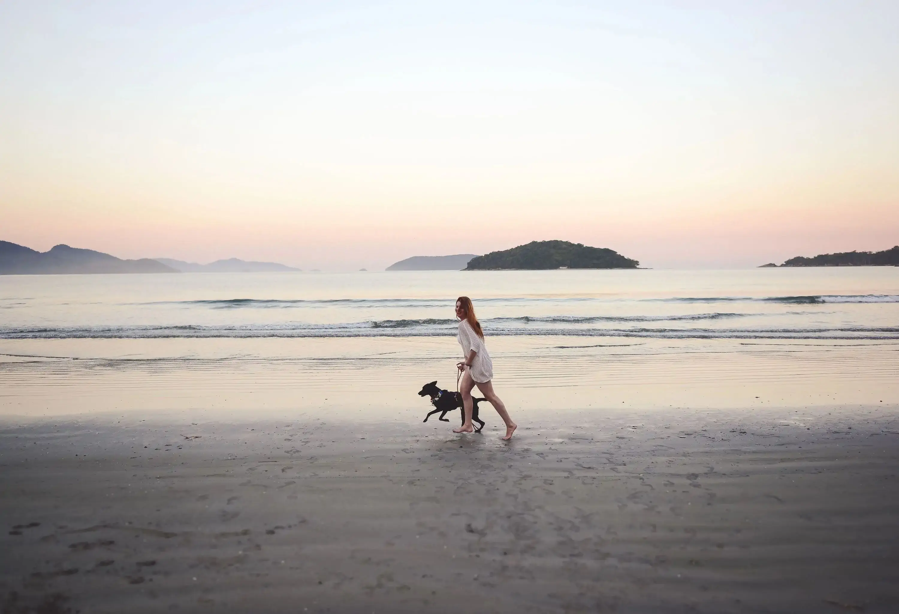 A young woman and her loyal dog joyfully run along the sandy beach as the sun sets.