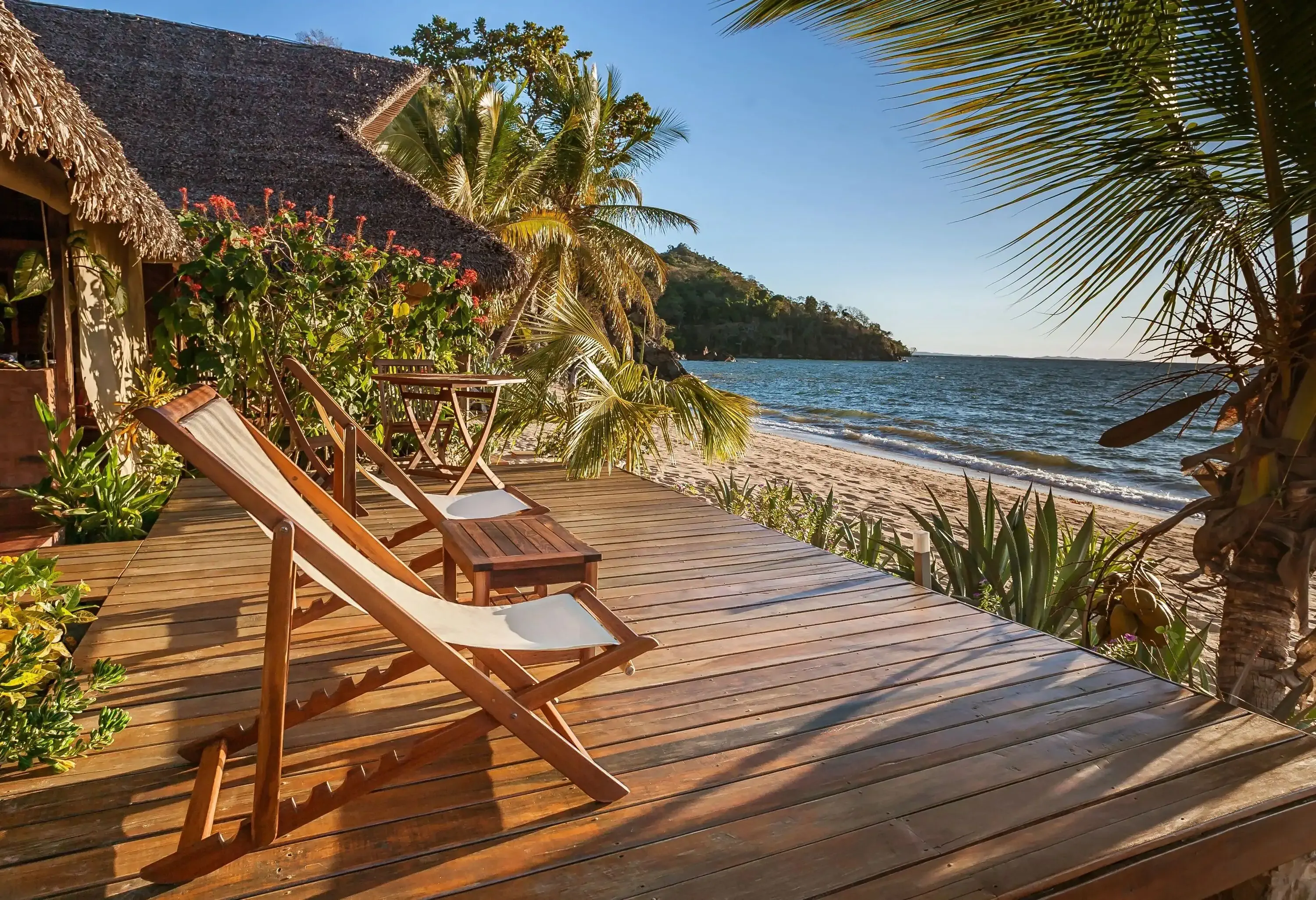 A small wooden terrace with deck chairs facing out into the beach.