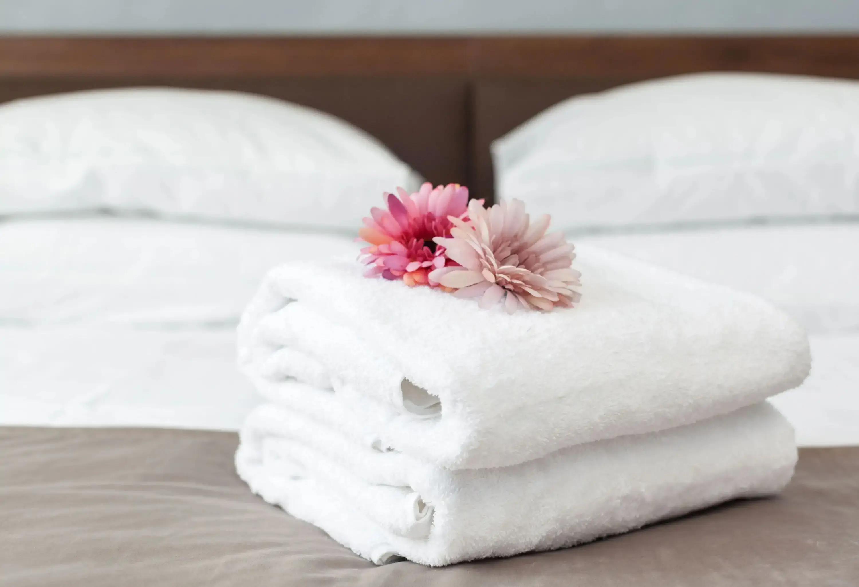 A stack of clean white towels in a bed topped with pink flowers.