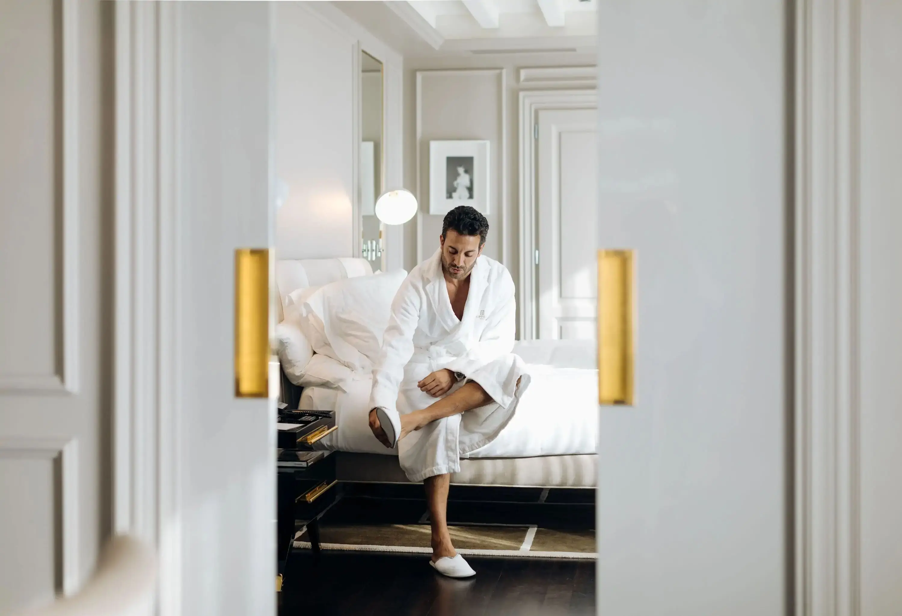 a man sitting on a hotelbed wearing a bathrobe and hotel slippers