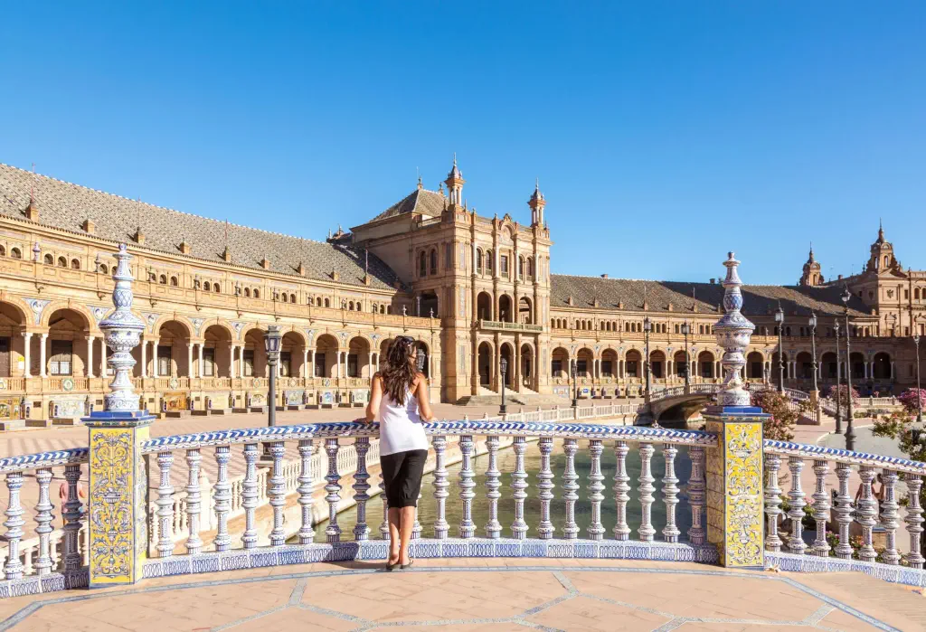 A woman leaning on the bridge balustrades, staring out into a plaza in front of a crescent-shaped monument.