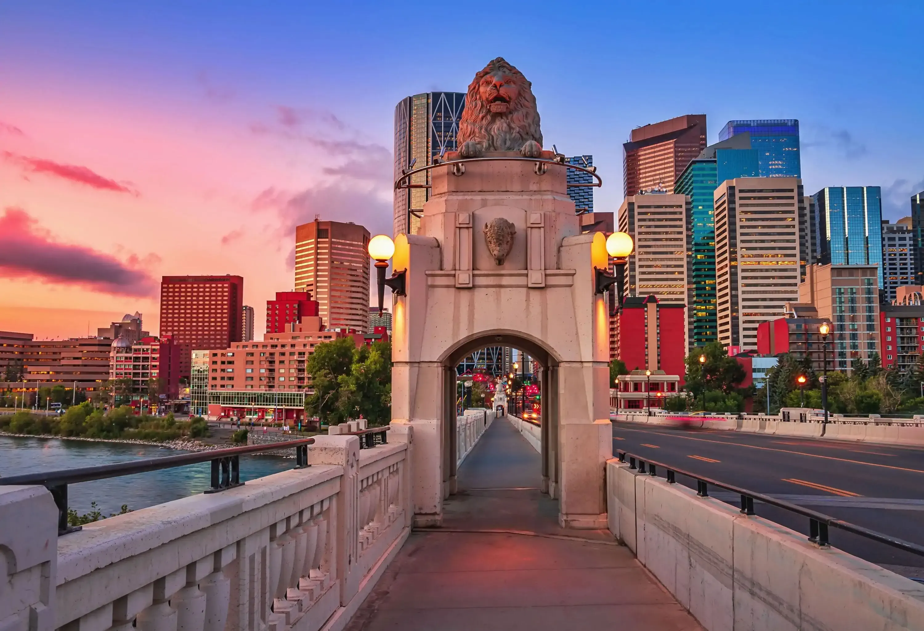A roadside walkway with a gateway monument of a lion statue towards a cluster of modern skyscrapers under a morning sky.