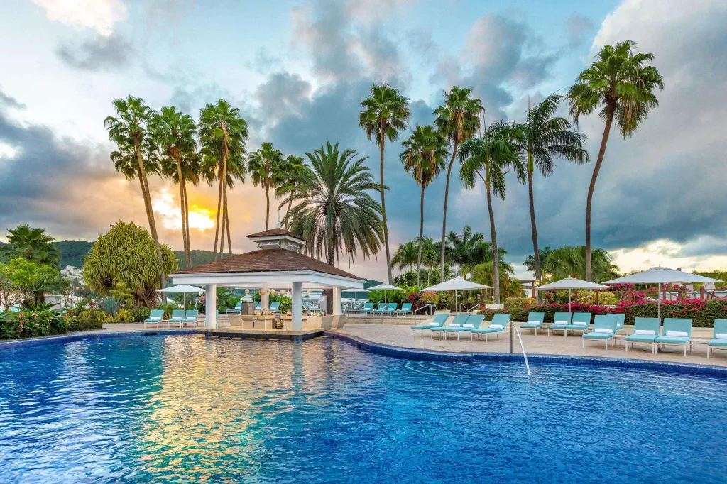Luxurious pool at sunset, surrounded by palm trees. Lounge chairs and umbrellas line the poolside, creating a relaxing, tropical ambiance.