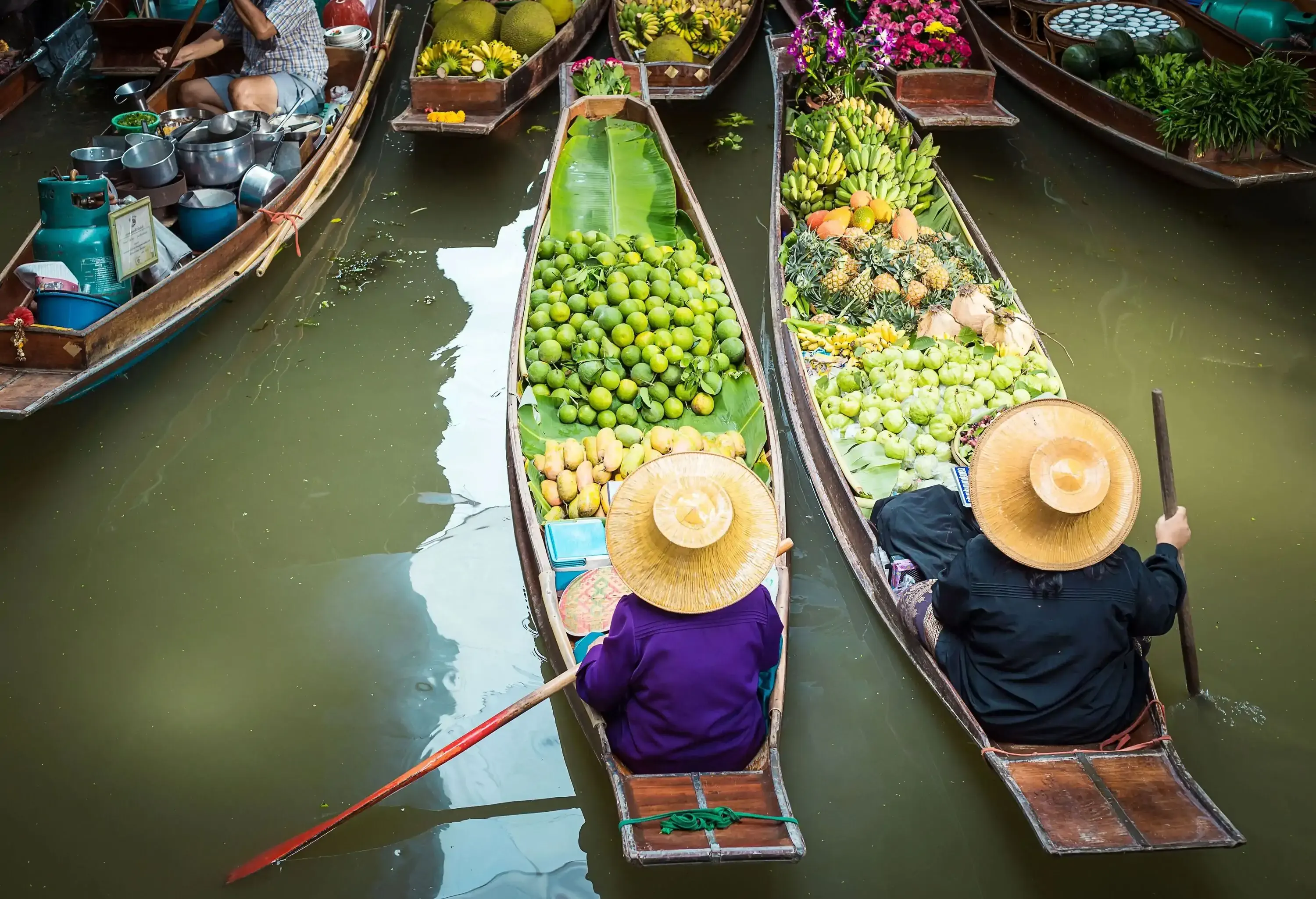 Vendors rowing wooden boats filled with fresh fruits and flowers.