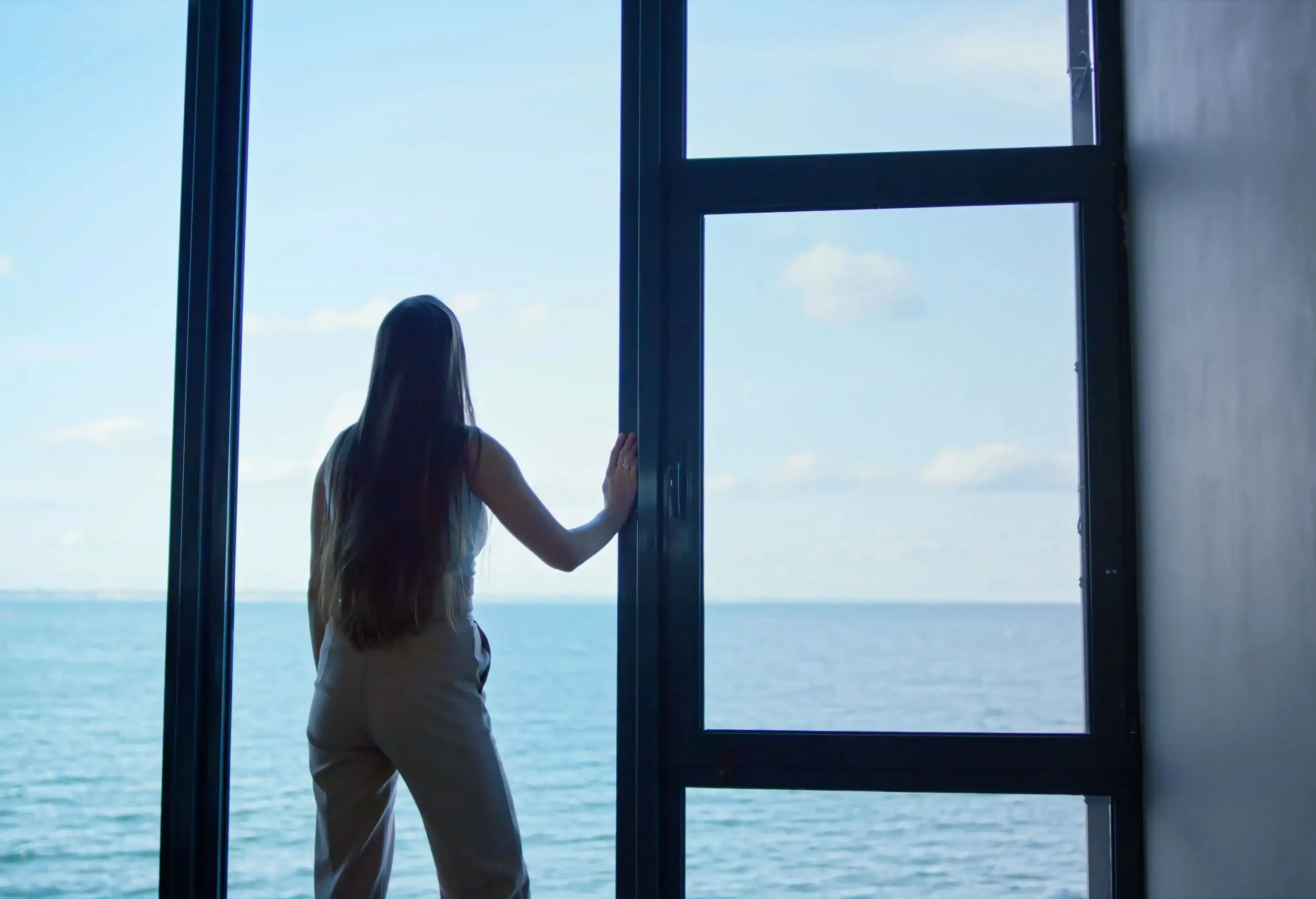 woman standing by a window looking out the ocean