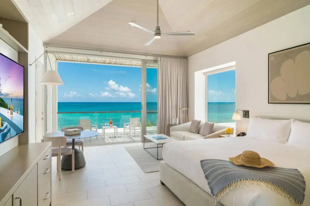 Bright and airy hotel room with ocean views, a plush bed, modern decor, and a cozy seating area overlooking the turquoise sea.