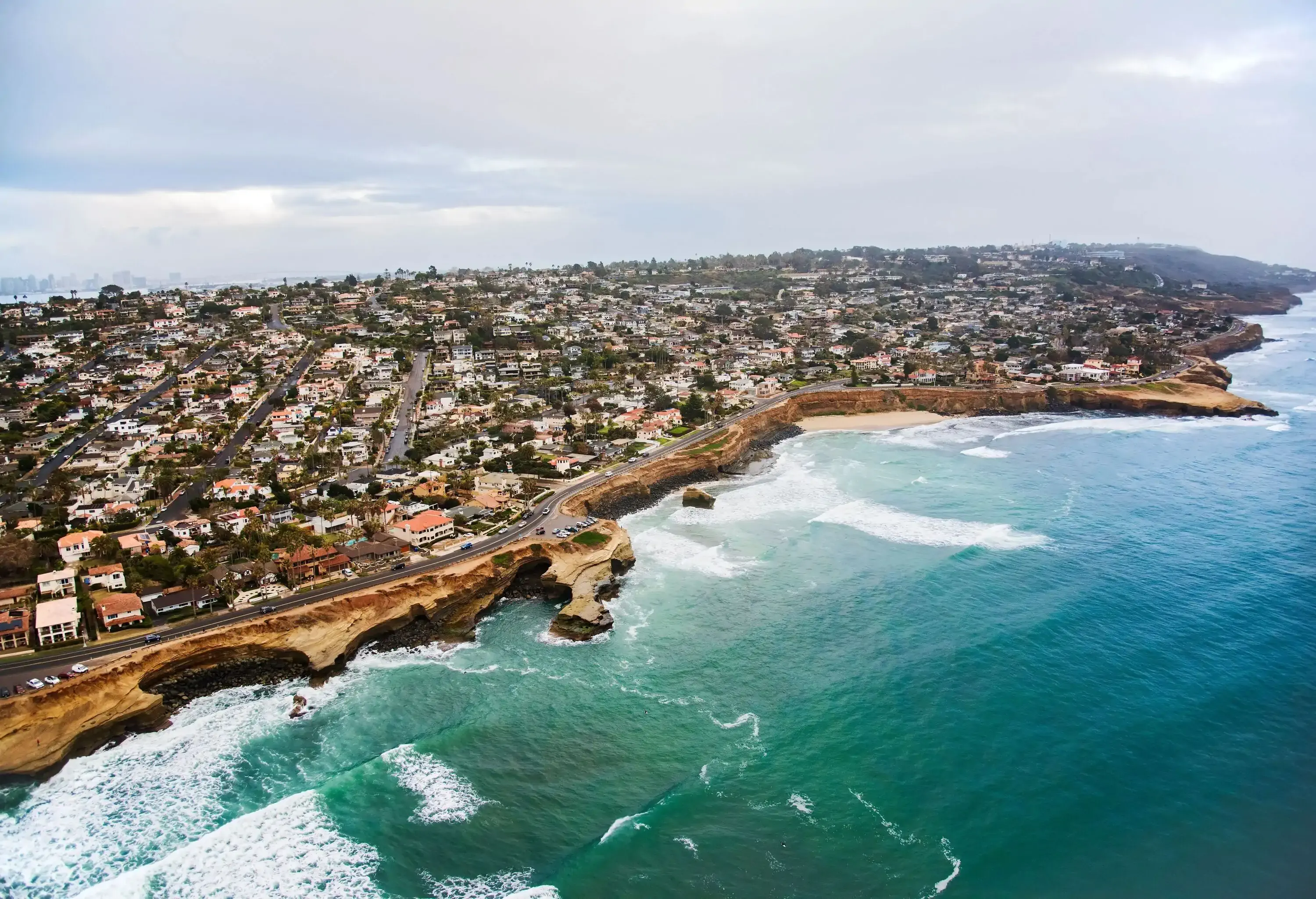 A large city atop a seaside cliff with faces carved by the waves.