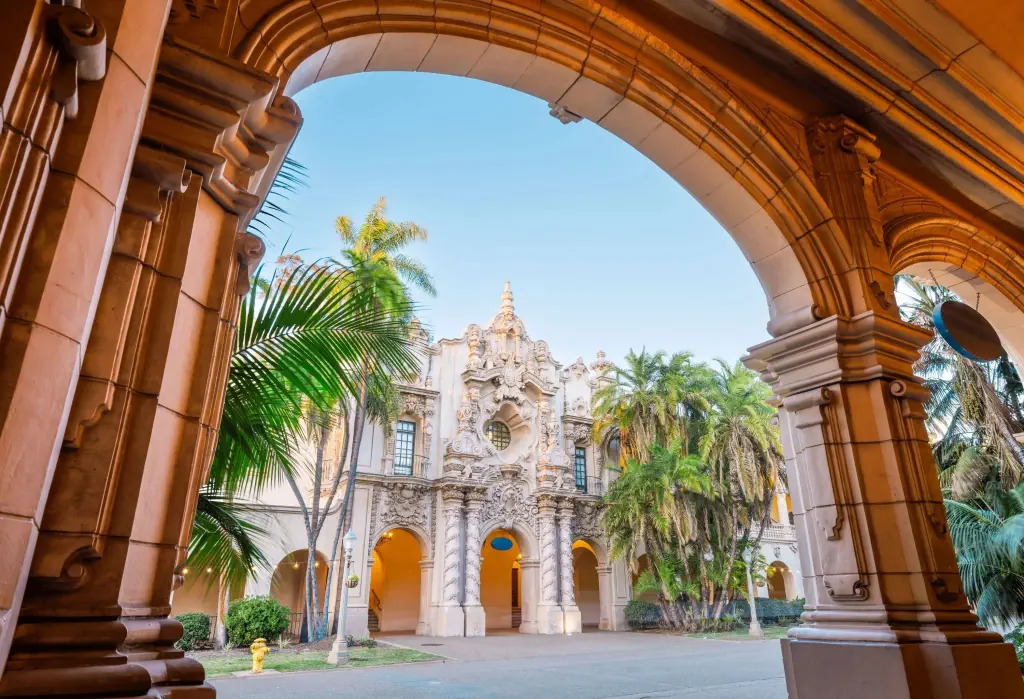 A grand, ornate building with intricate carvings and arches, viewed through a stone archway lined with columns.